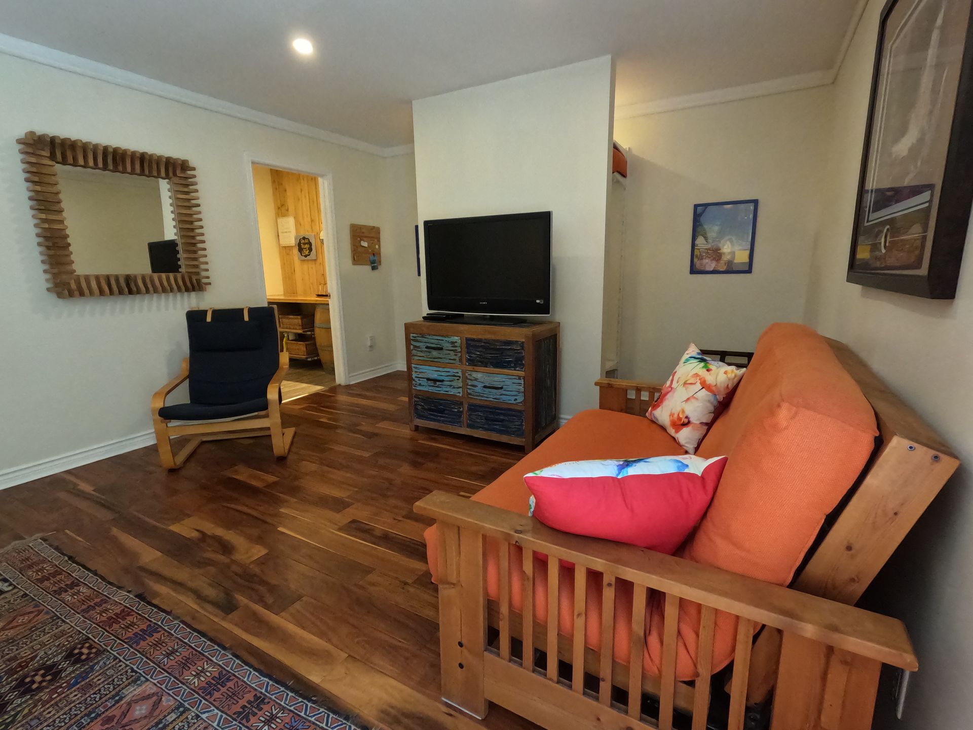 Cozy living room with orange sofa, blue chair, TV stand, and hardwood floors