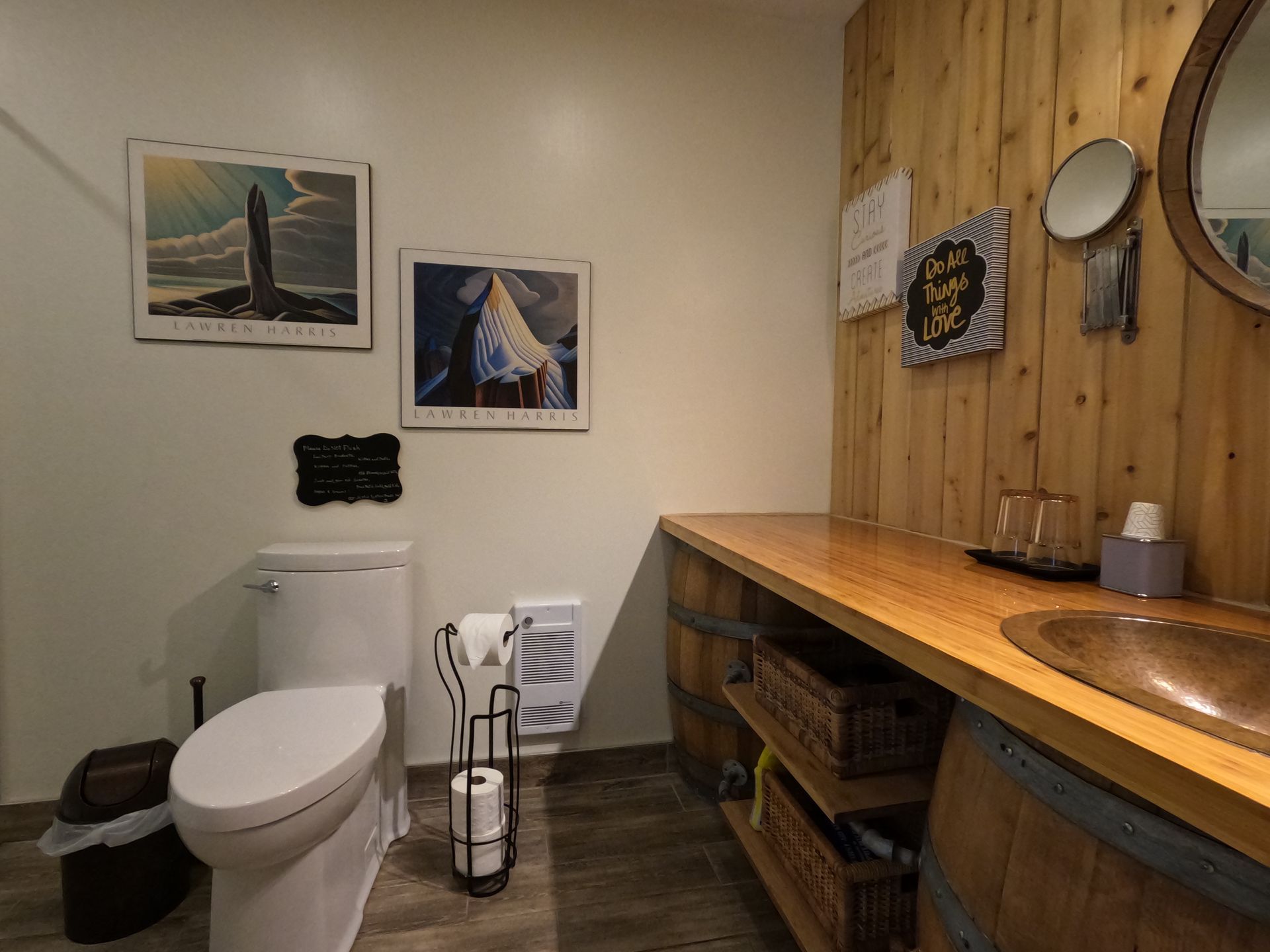 Small restroom with toilet, sink counter, wood-paneled wall, and framed pictures above the toilet.