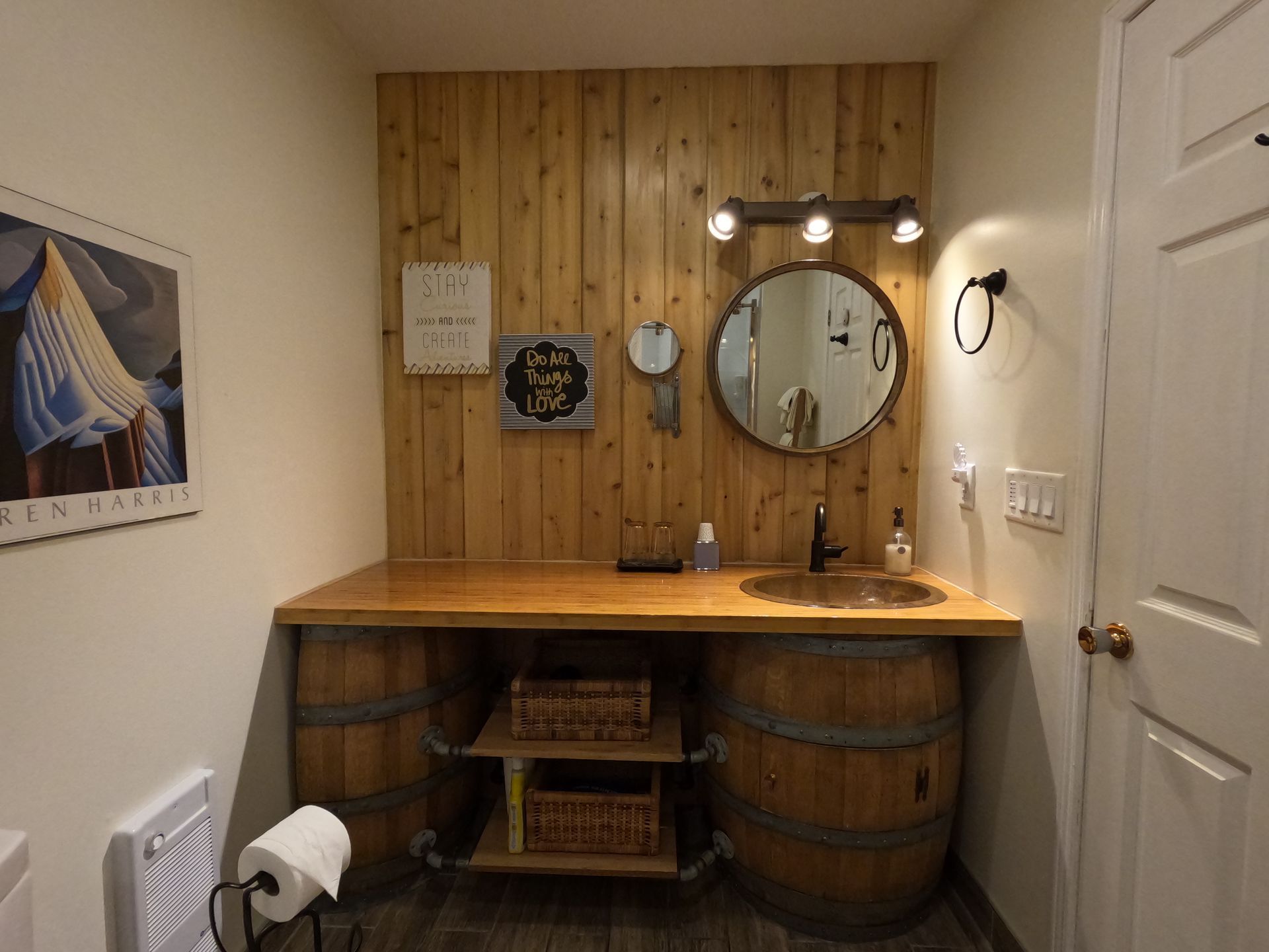 Small rustic bathroom with wood-paneled vanity, round mirror, barrel sink, and toilet paper holder on the left.