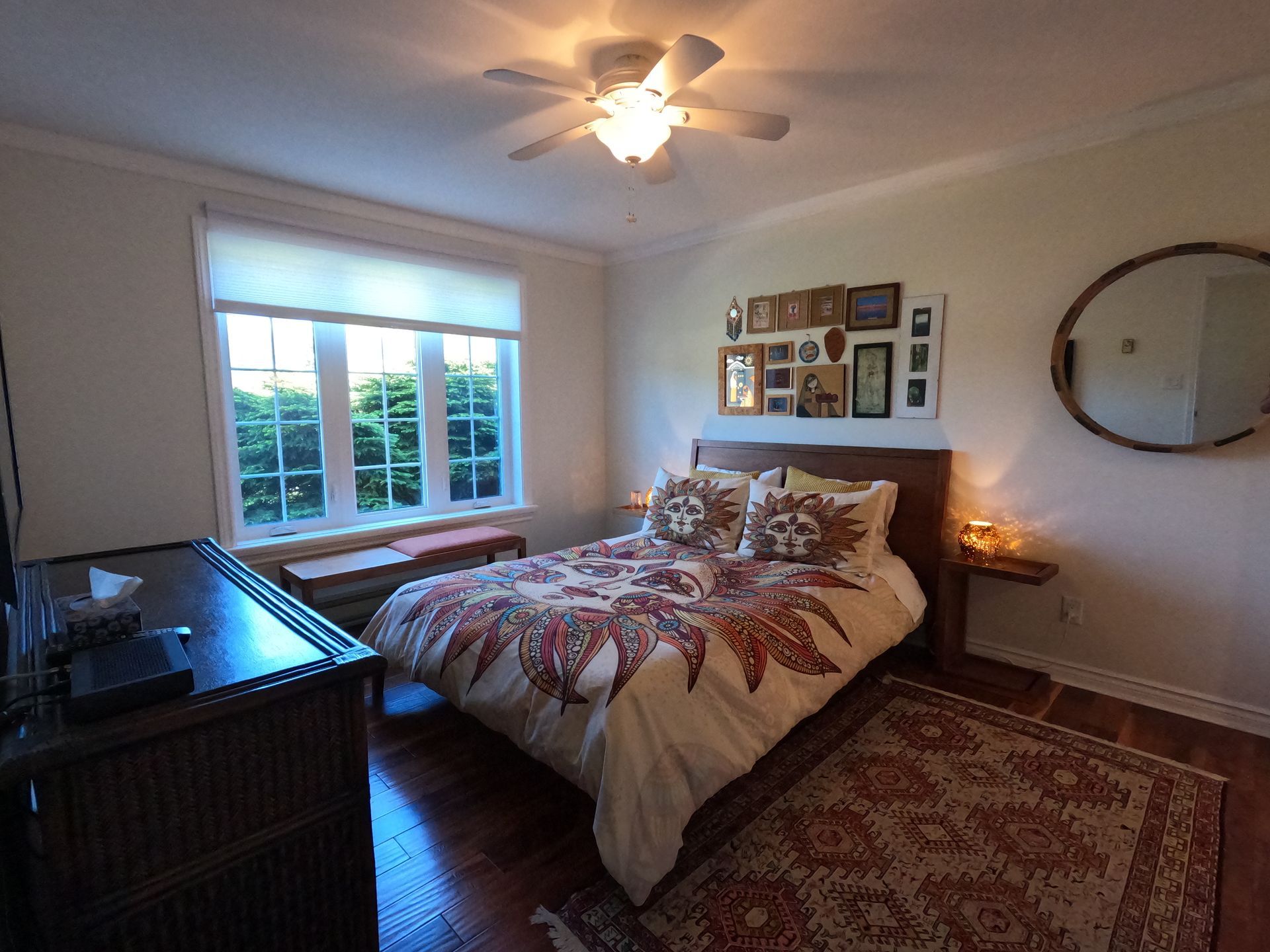 Cozy bedroom with a bed, rug, dresser, window, and ceiling fan in warm light