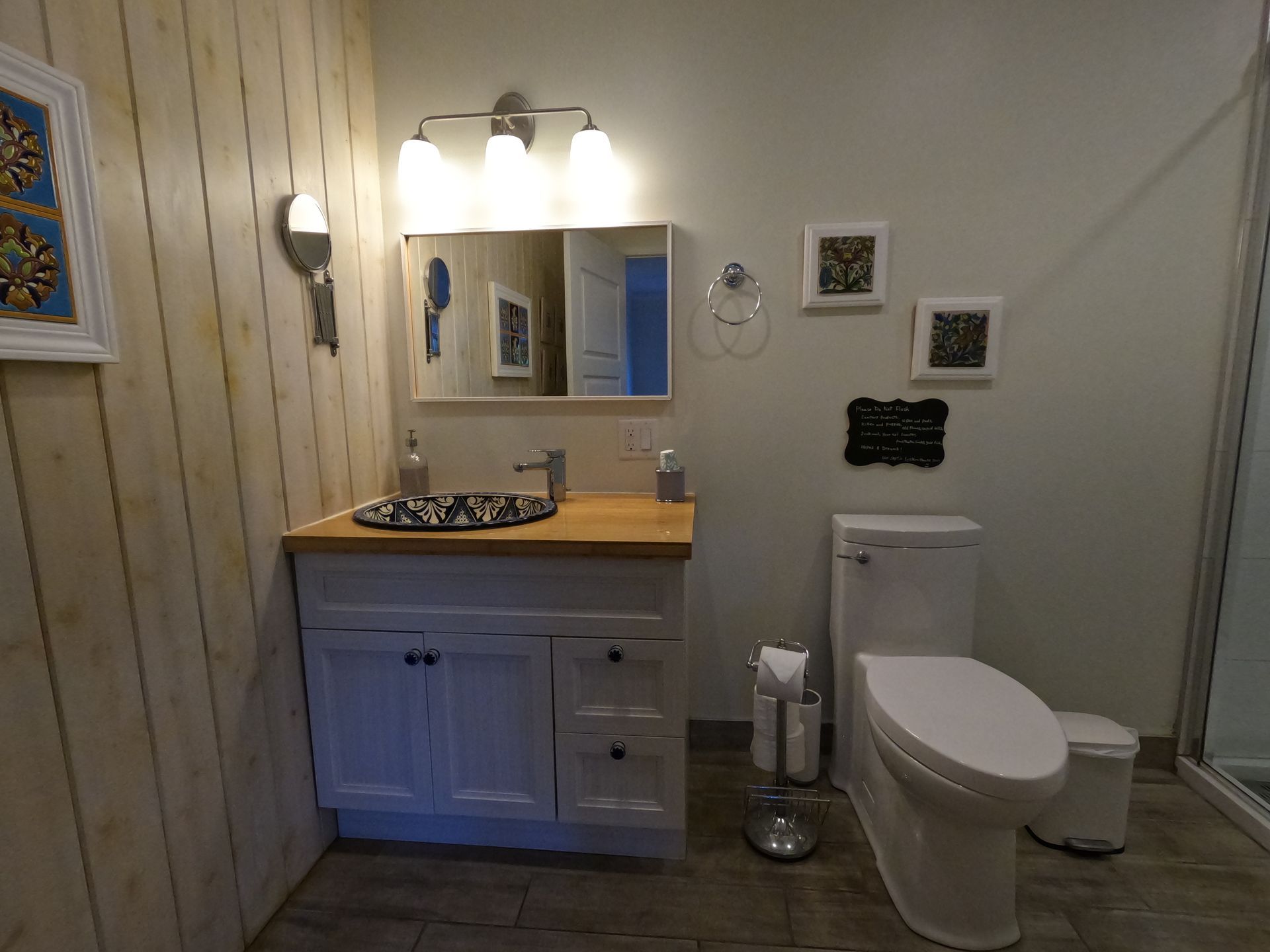 Small bathroom with white vanity, mirror lights, toilet, and wood accent wall.