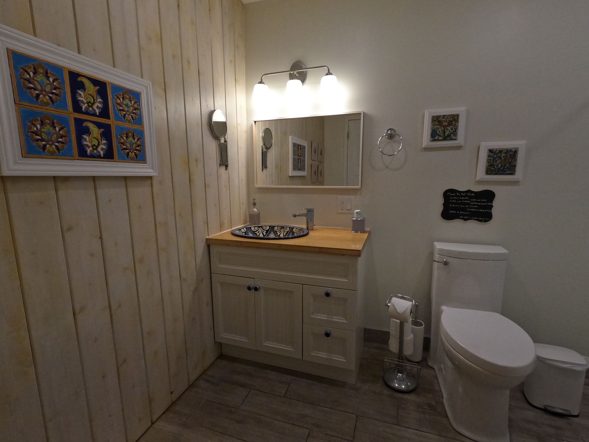 Bathroom with wood-paneled walls, vanity sink, toilet, mirror, and wall sconces