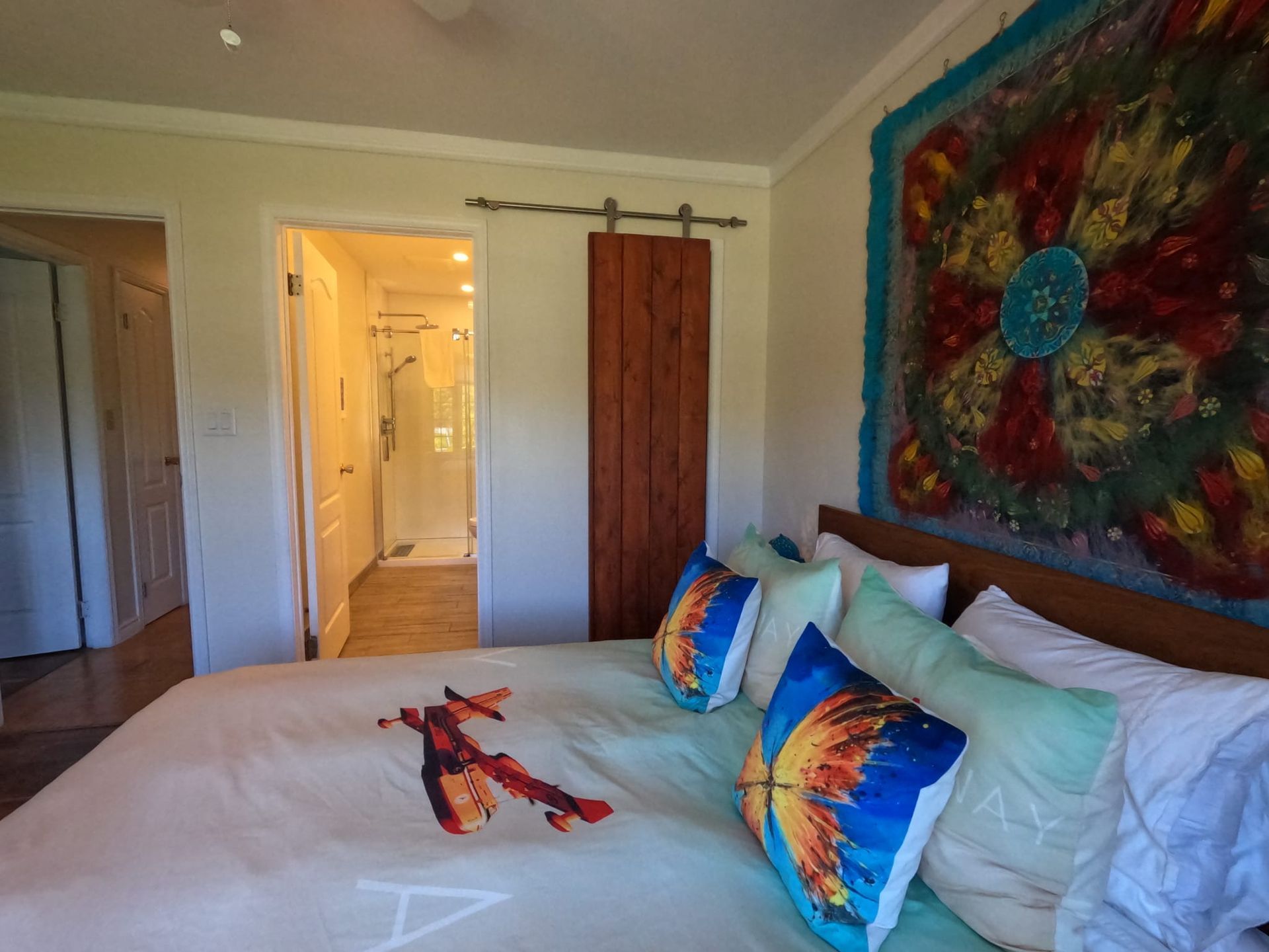 Bedroom with colorful wall art, white bed, and open doorway to a lit hallway