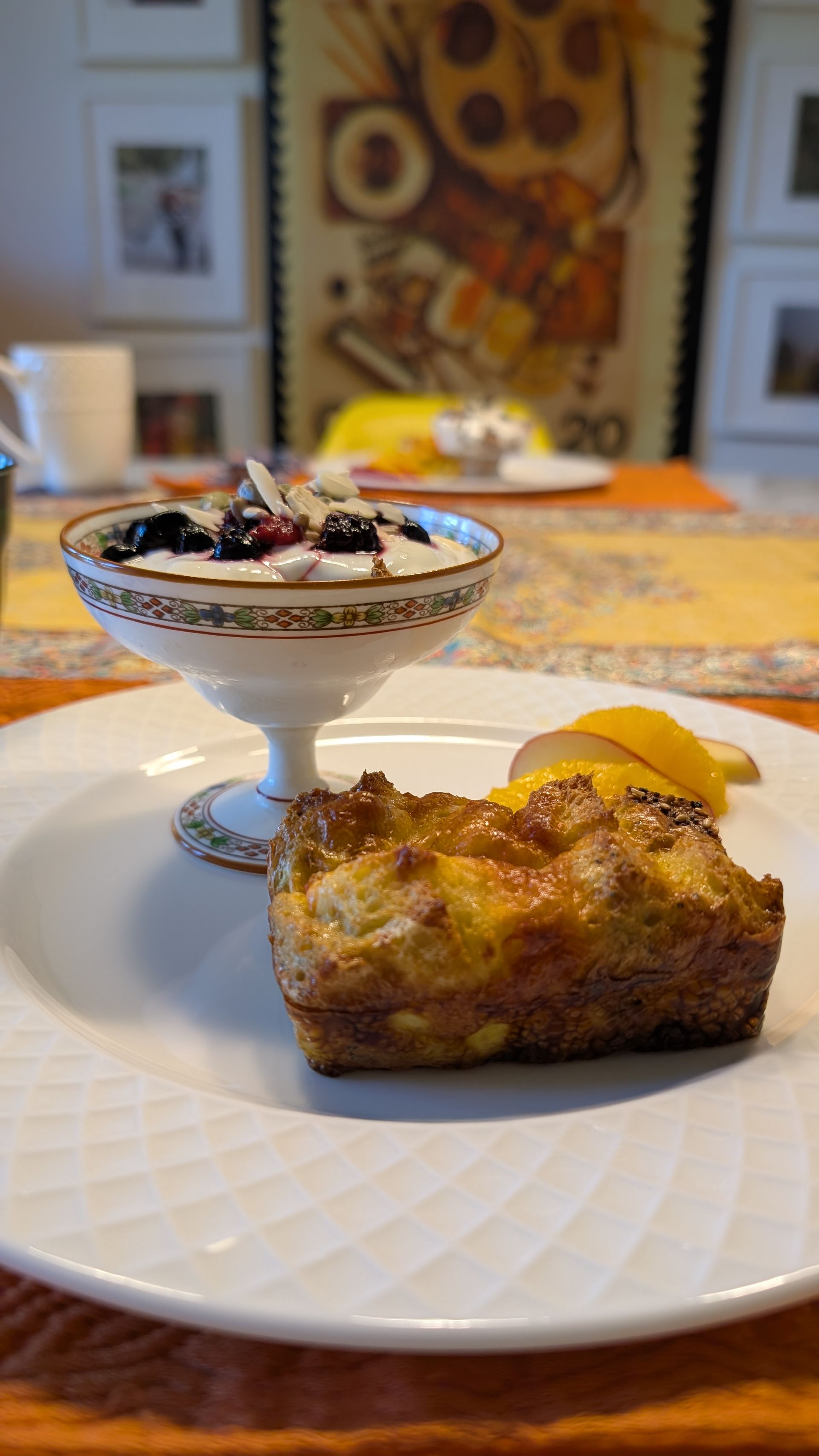 Breakfast plate with a bread pudding slice and a bowl of berry-topped yogurt on a table