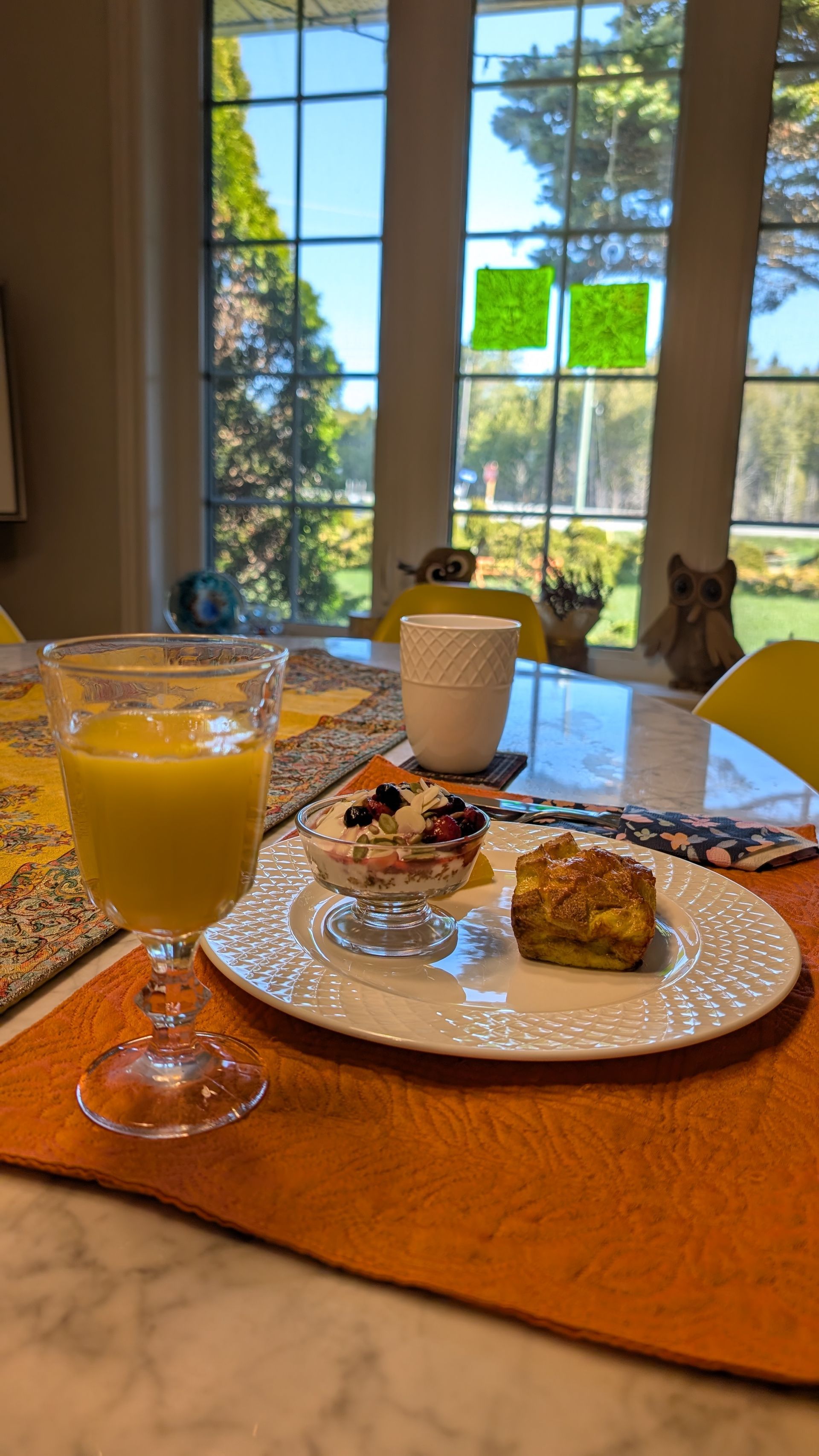Breakfast table with orange juice, coffee, pastry, and a bright window view