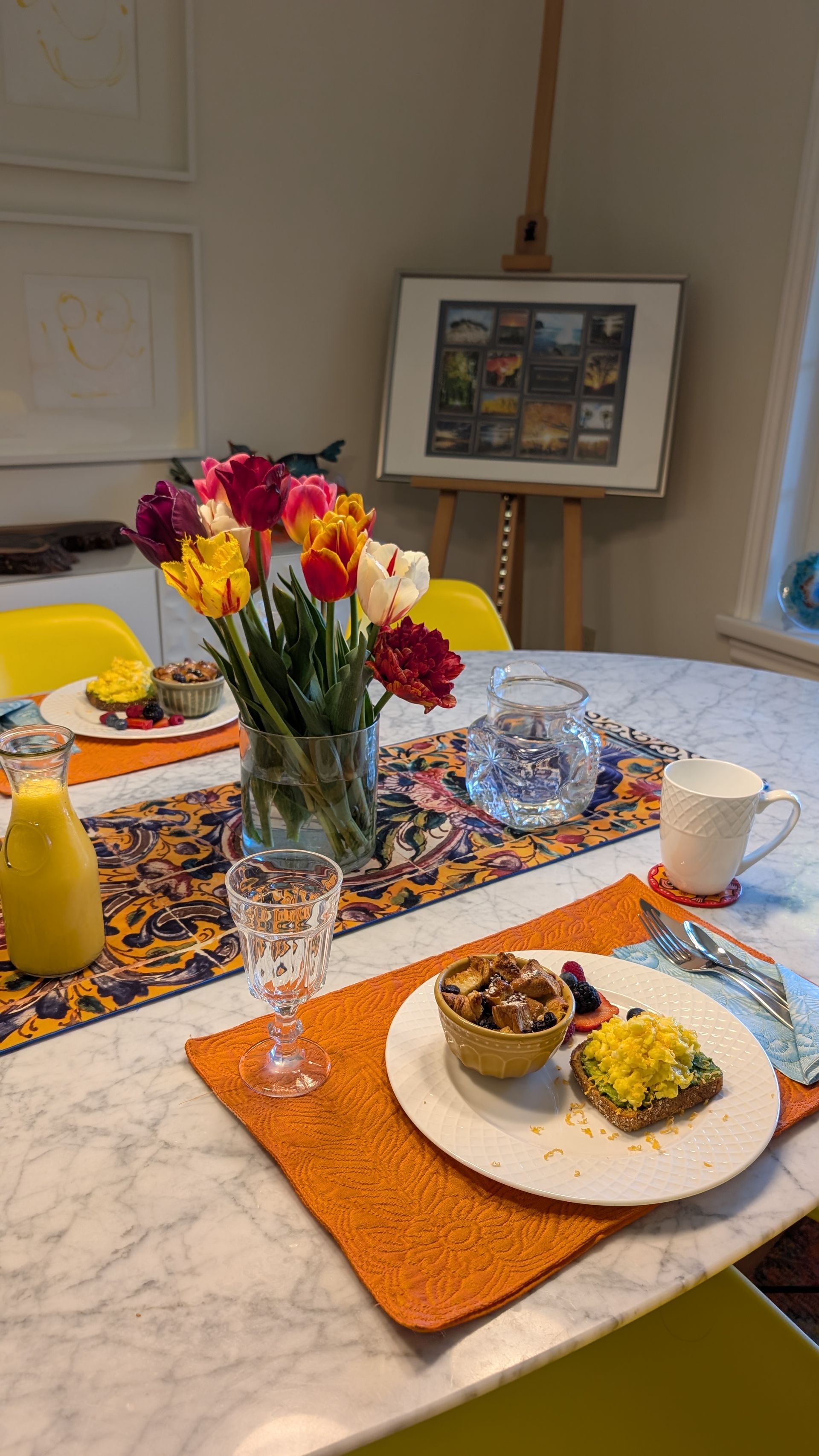 Table set with colorful flowers, breakfast plates, and a candle in a bright dining room
