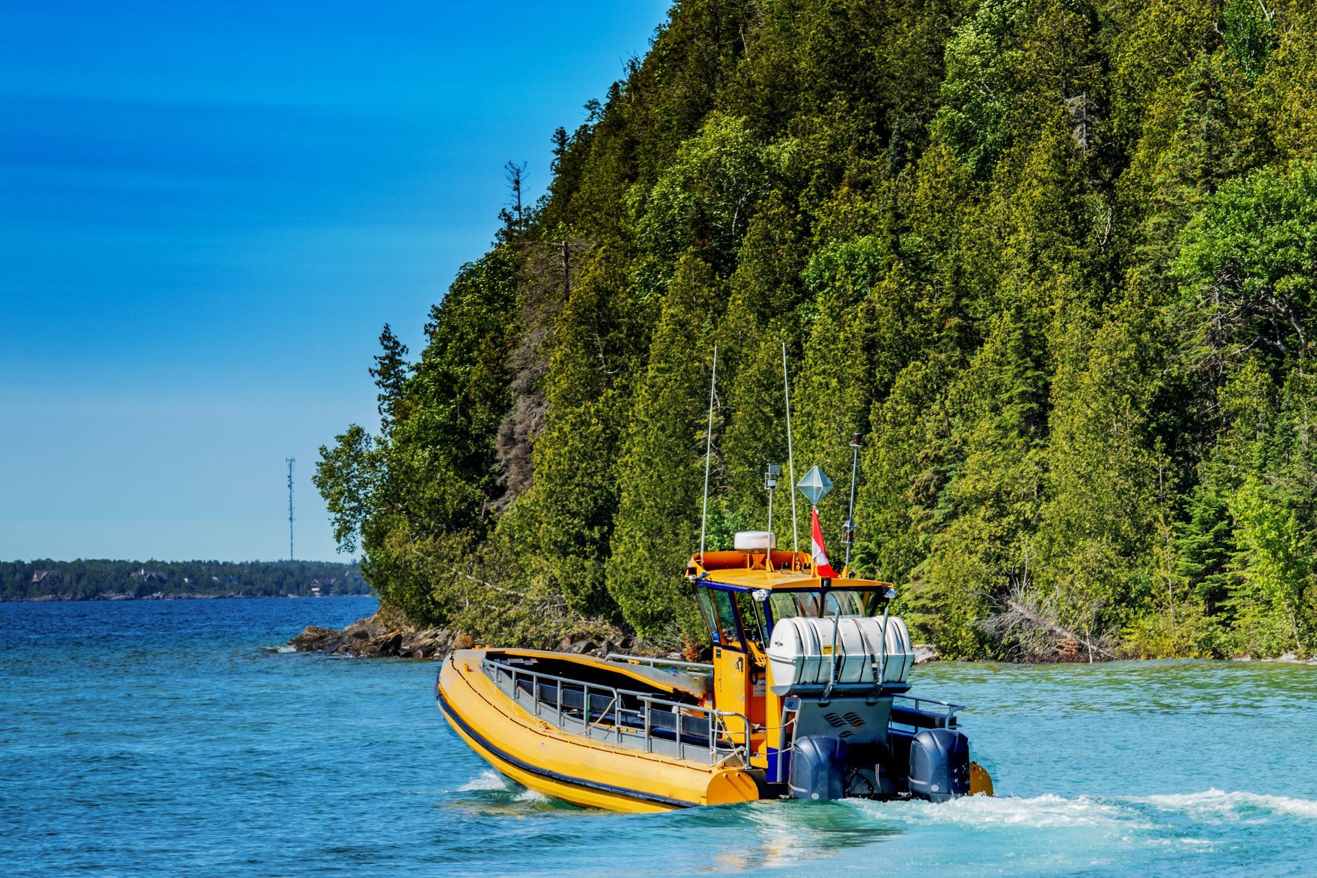 Yellow boat speeding past a forested shoreline on blue water under a clear sky