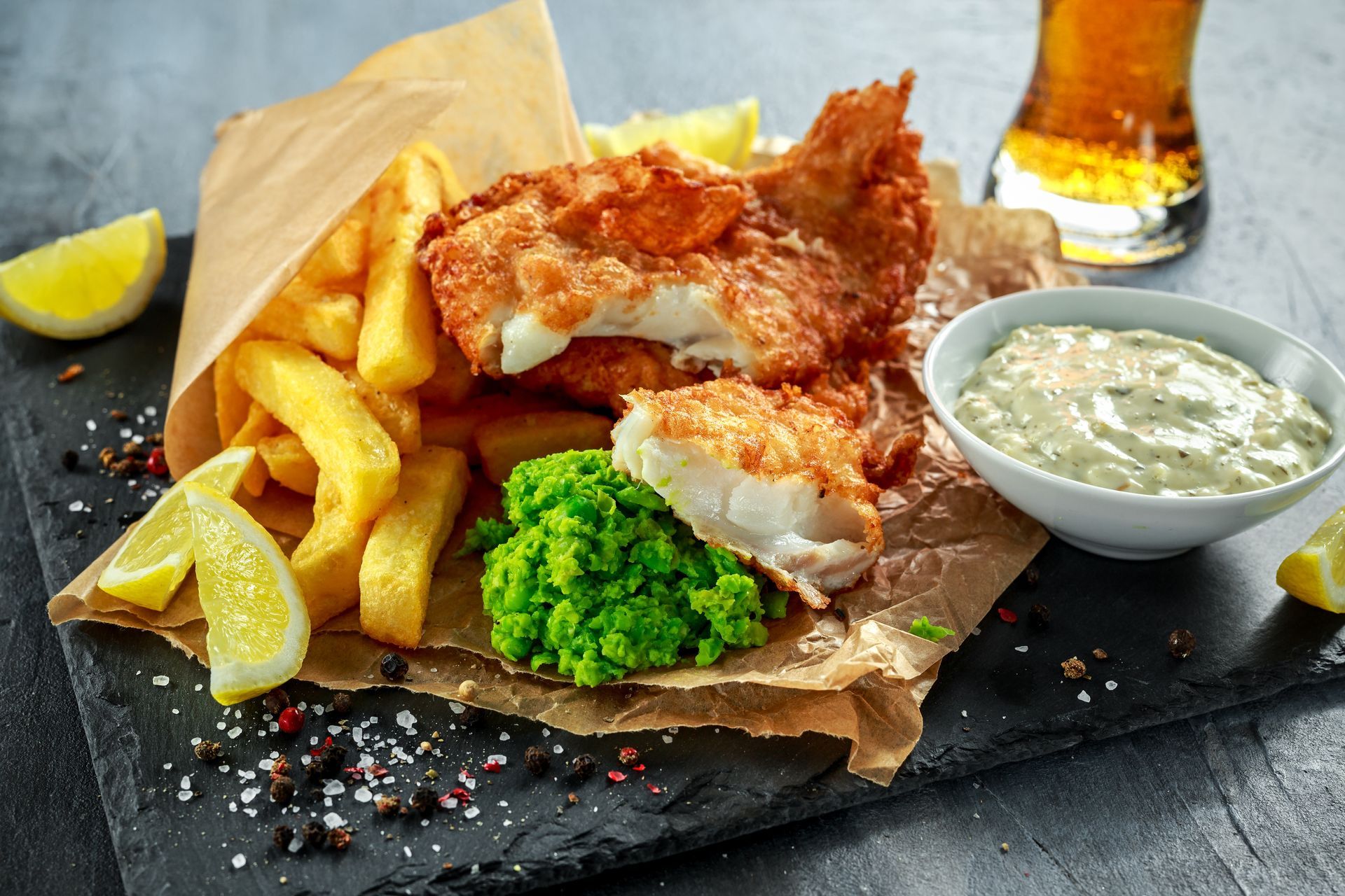 Fish and chips with lemon wedges, mushy peas, and tartar sauce on parchment paper