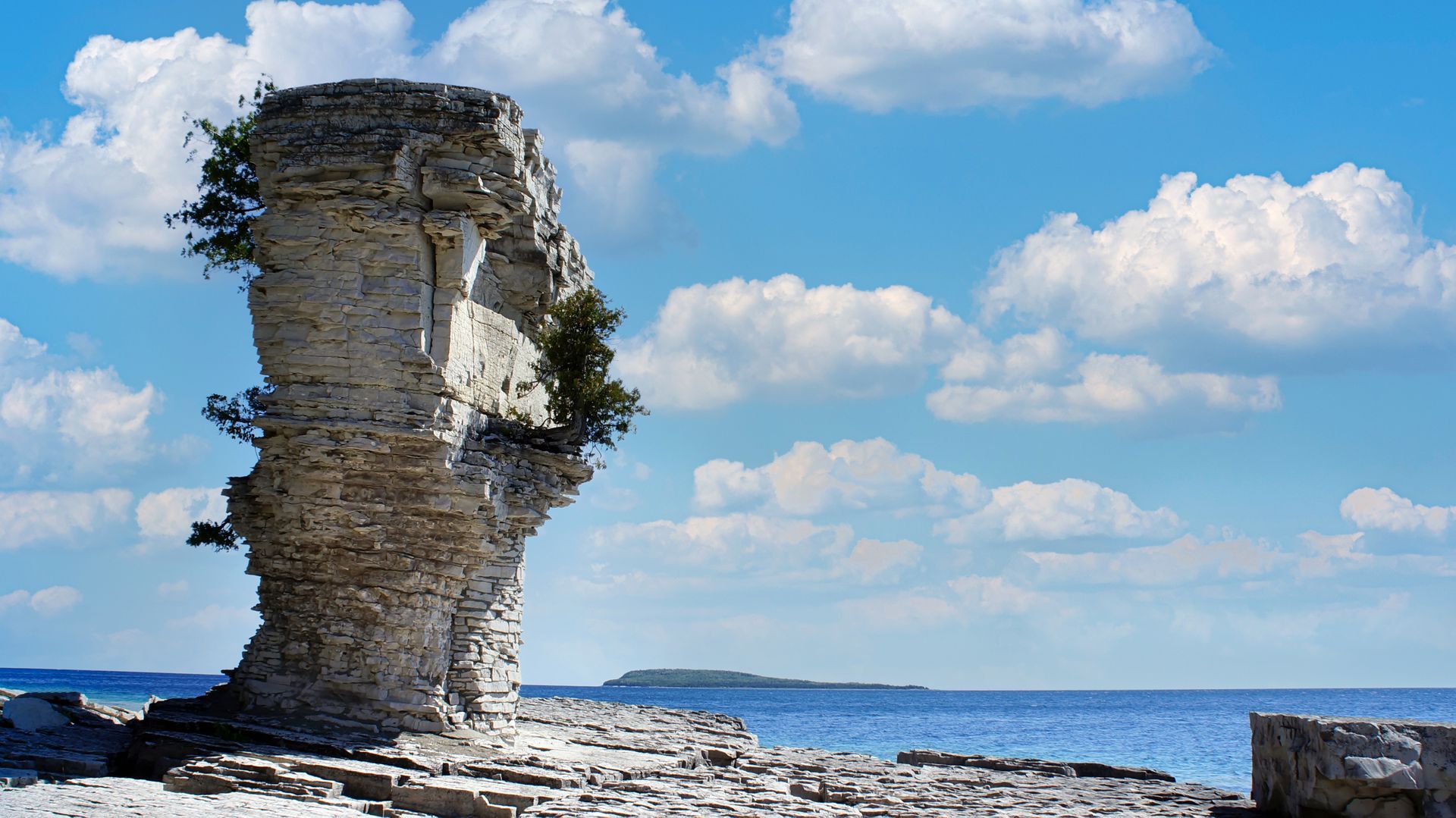 Weathered limestone sea stack beside a blue ocean under a partly cloudy sky