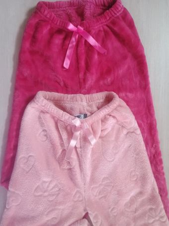 Dos pantalones rosas de felpa con cordón ajustable apilados verticalmente sobre un fondo gris.