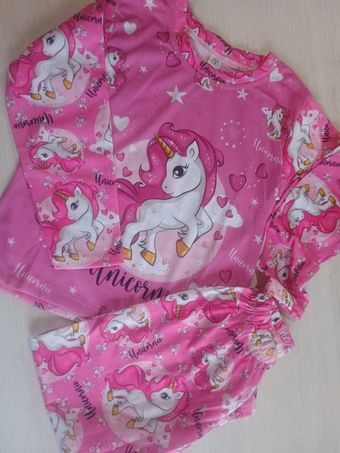 Conjunto de pijama infantil rosa con estampado de unicornio, de manga larga y pantalón corto sobre fondo claro.
