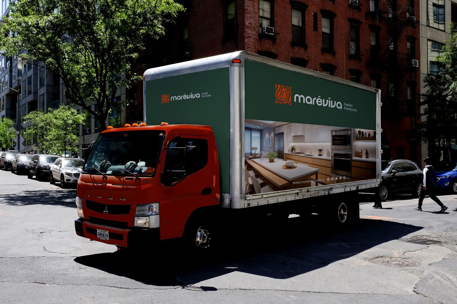 Um caminhão de entregas laranja percorre uma rua da cidade, com a lateral decorada com a foto de uma cozinha moderna.