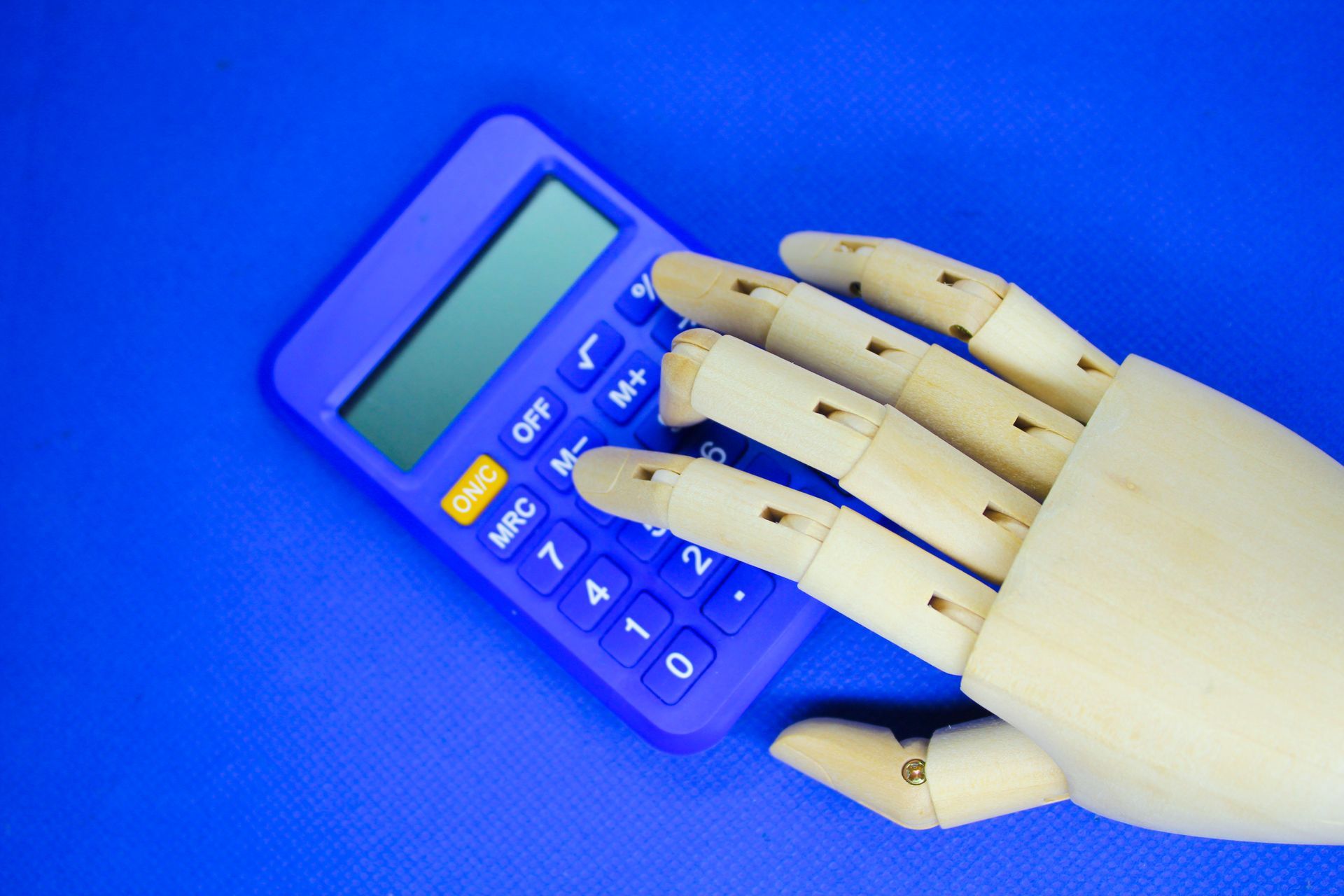 Uma mão de madeira está usando uma calculadora roxa em um fundo azul