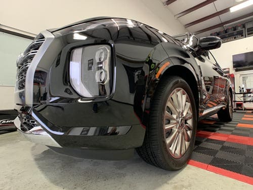 A low-angle view of the front corner of a black SUV parked inside a garage with red and black floor tiles.