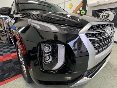 Front angle of a glossy black Hyundai Palisade parked inside a shop with a tiled floor.