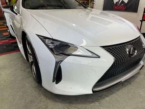 White Lexus sedan in a garage, front-left view, with a large black grille and sharp headlights.