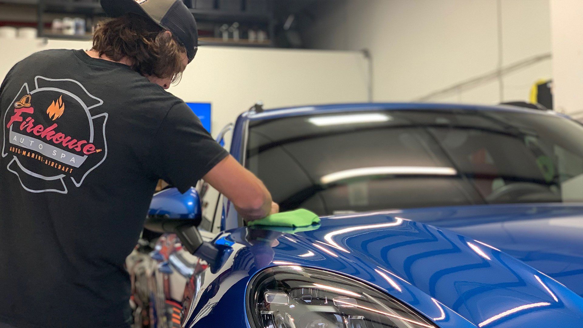 Person cleaning a blue sports car in a garage, using a cloth on the hood.