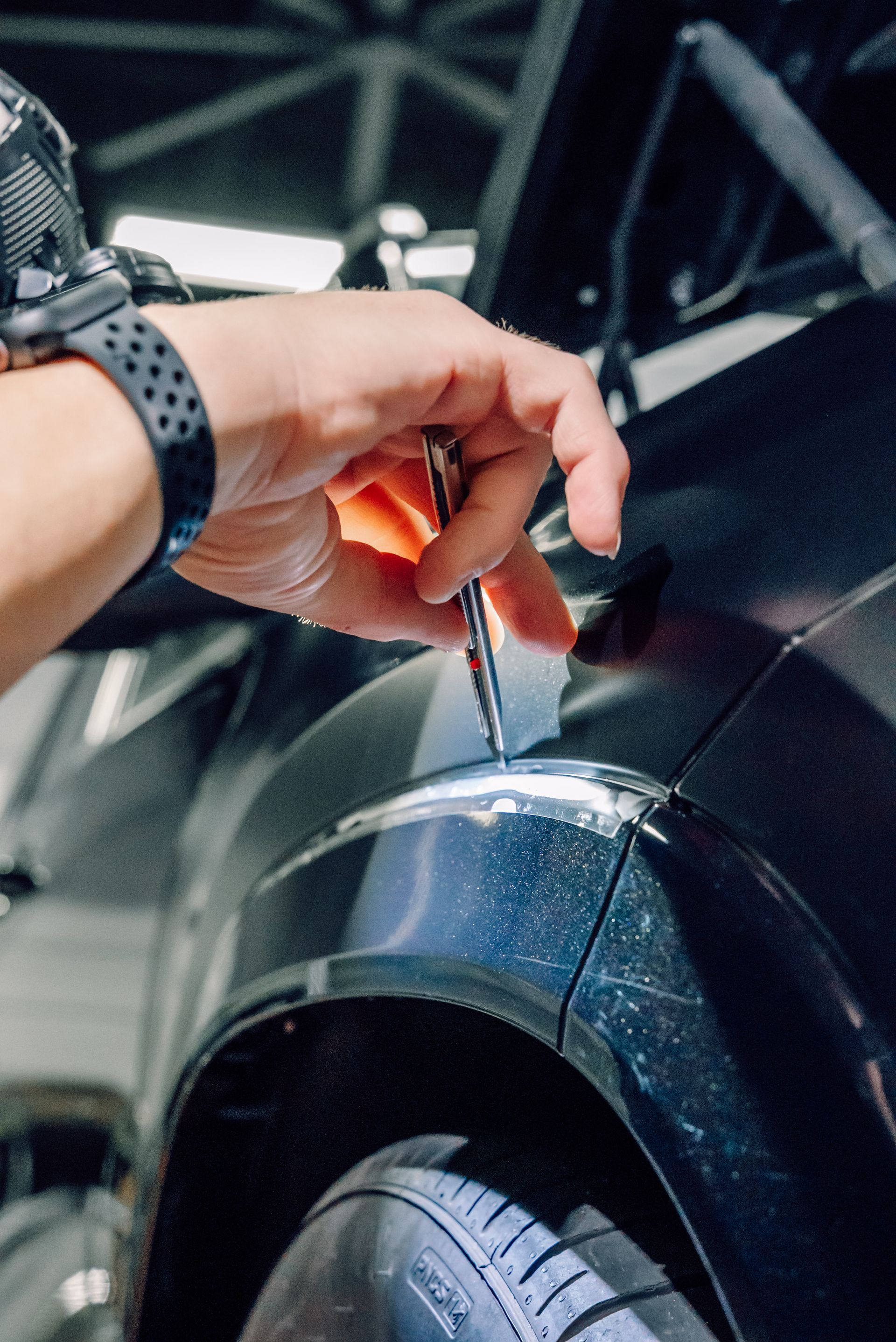 Hand holding a screwdriver over a black car wheel arch, tightening a fastener