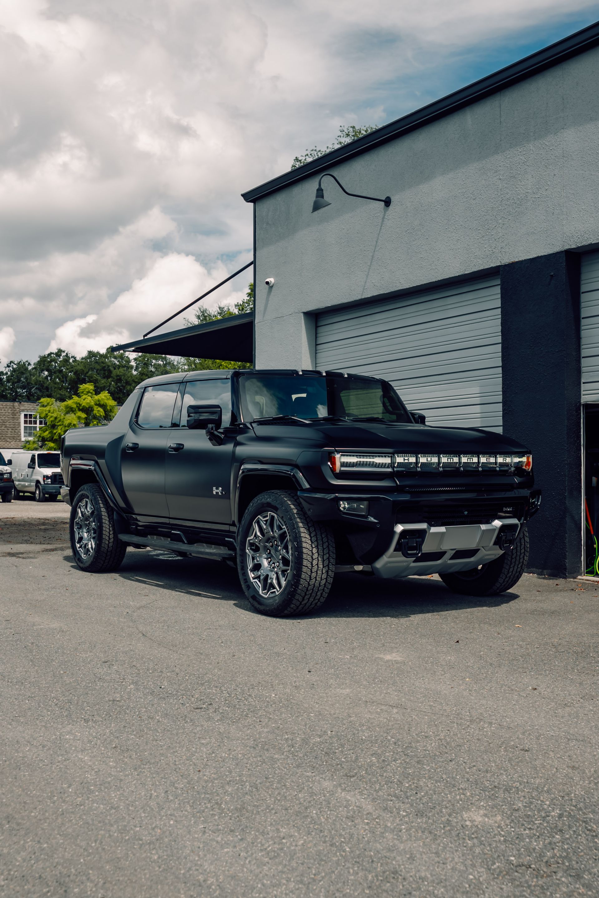 Black lifted pickup truck parked beside a gray industrial building under cloudy skies