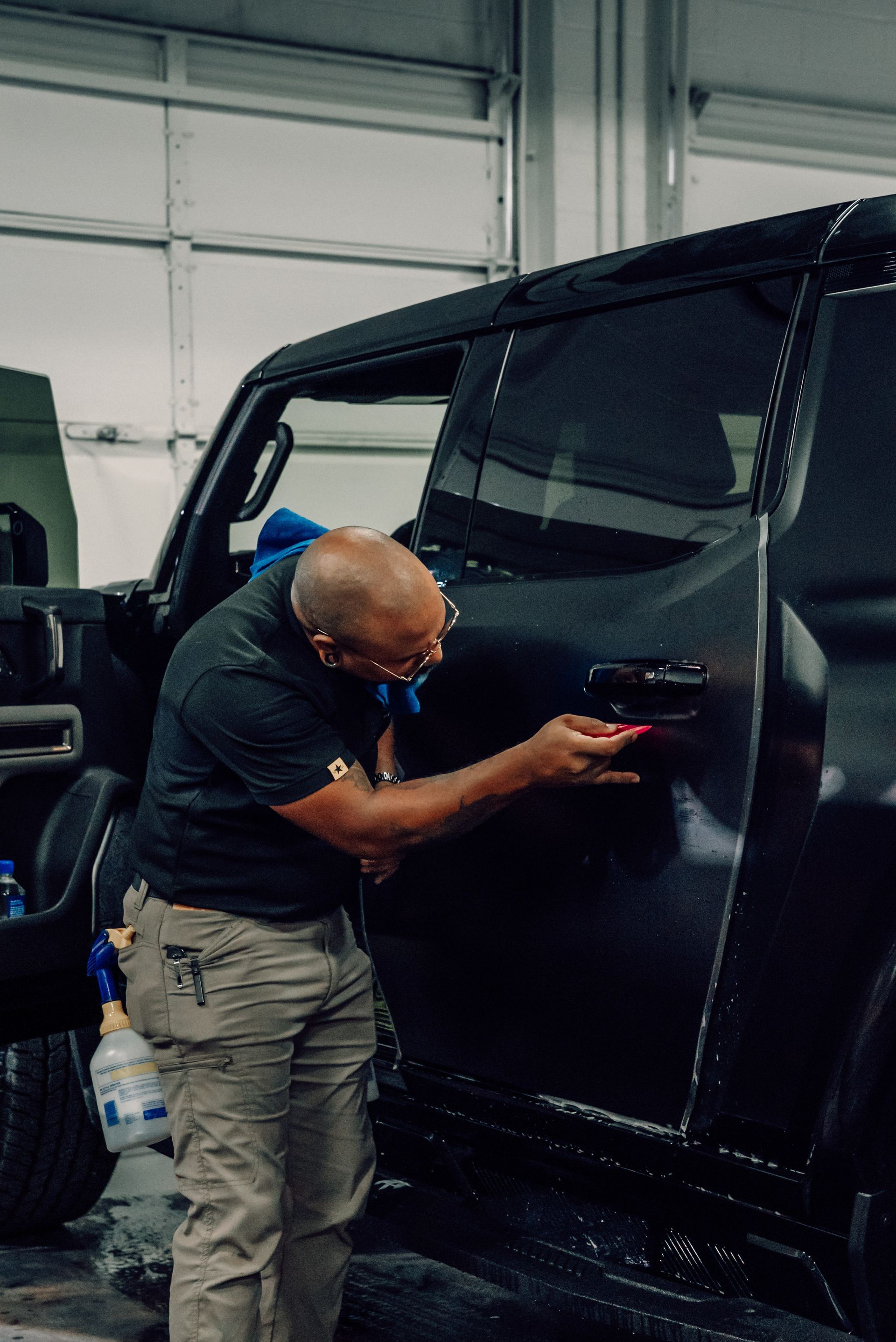 Man polishing a black vehicle door inside a garage with a cloth