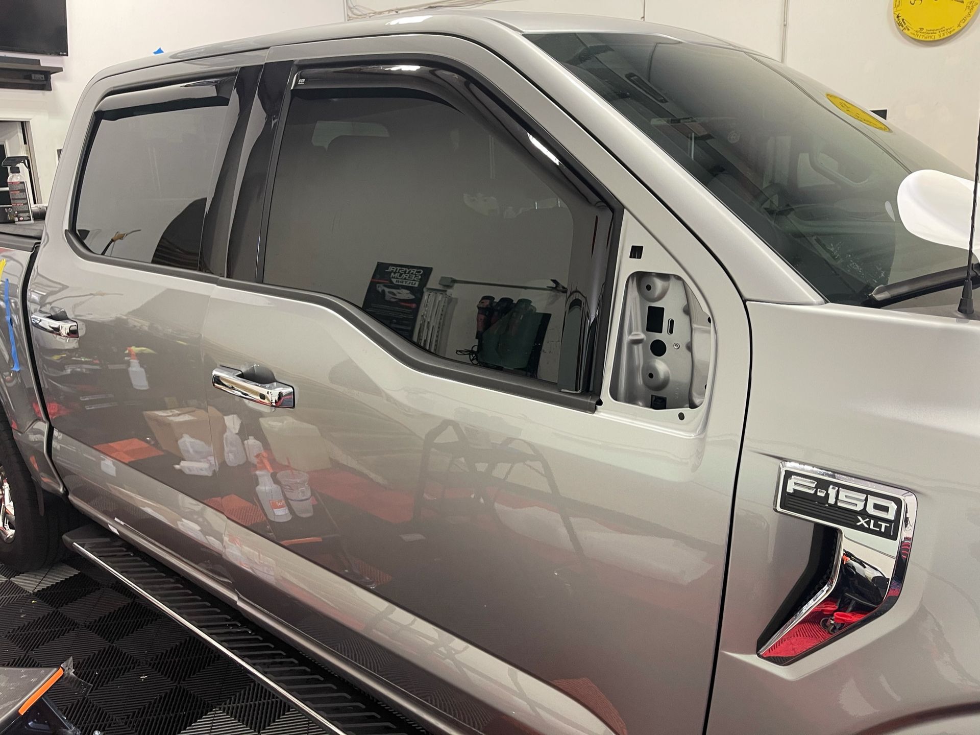 Silver Ford F-150 truck with tinted windows, missing side mirror. Inside a workshop setting.