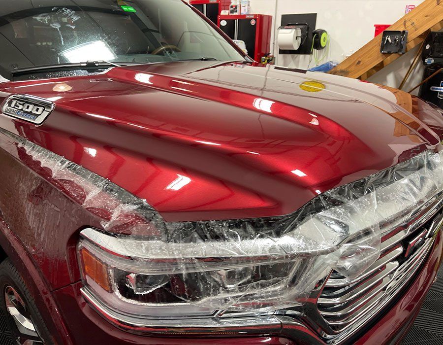 A red truck is covered in plastic wrap in a garage.
