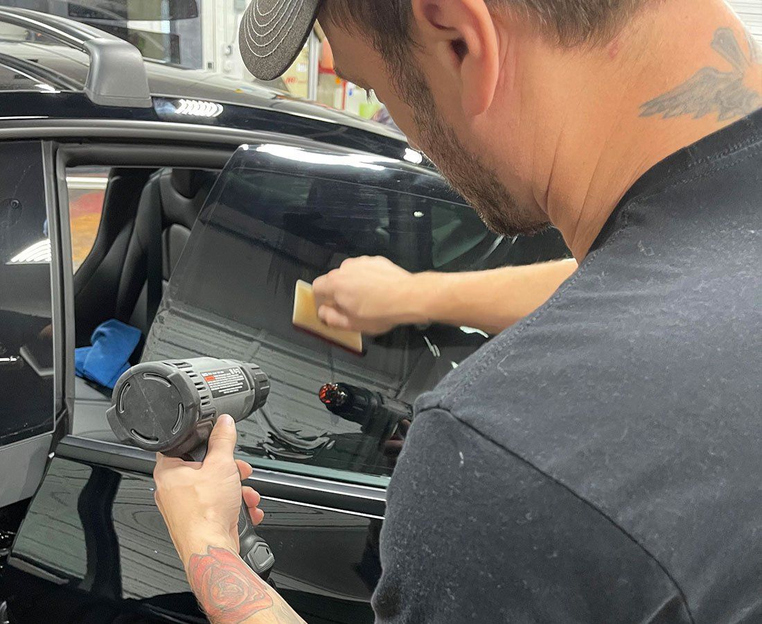 Man cleaning a car window with a cloth while holding a handheld tool near the door