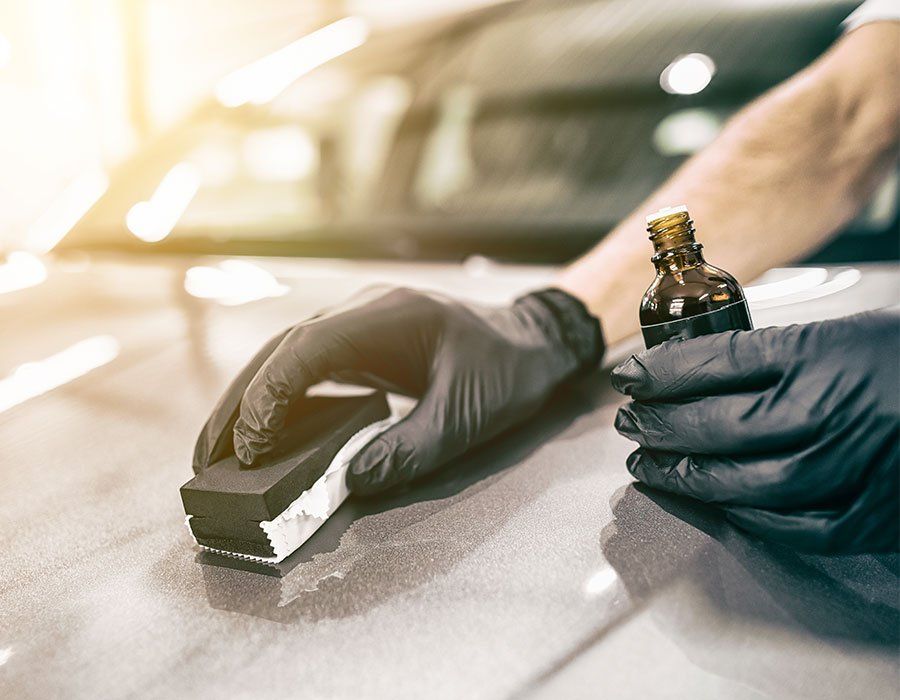 Gloved hands using a polishing block and bottle to detail a car surface