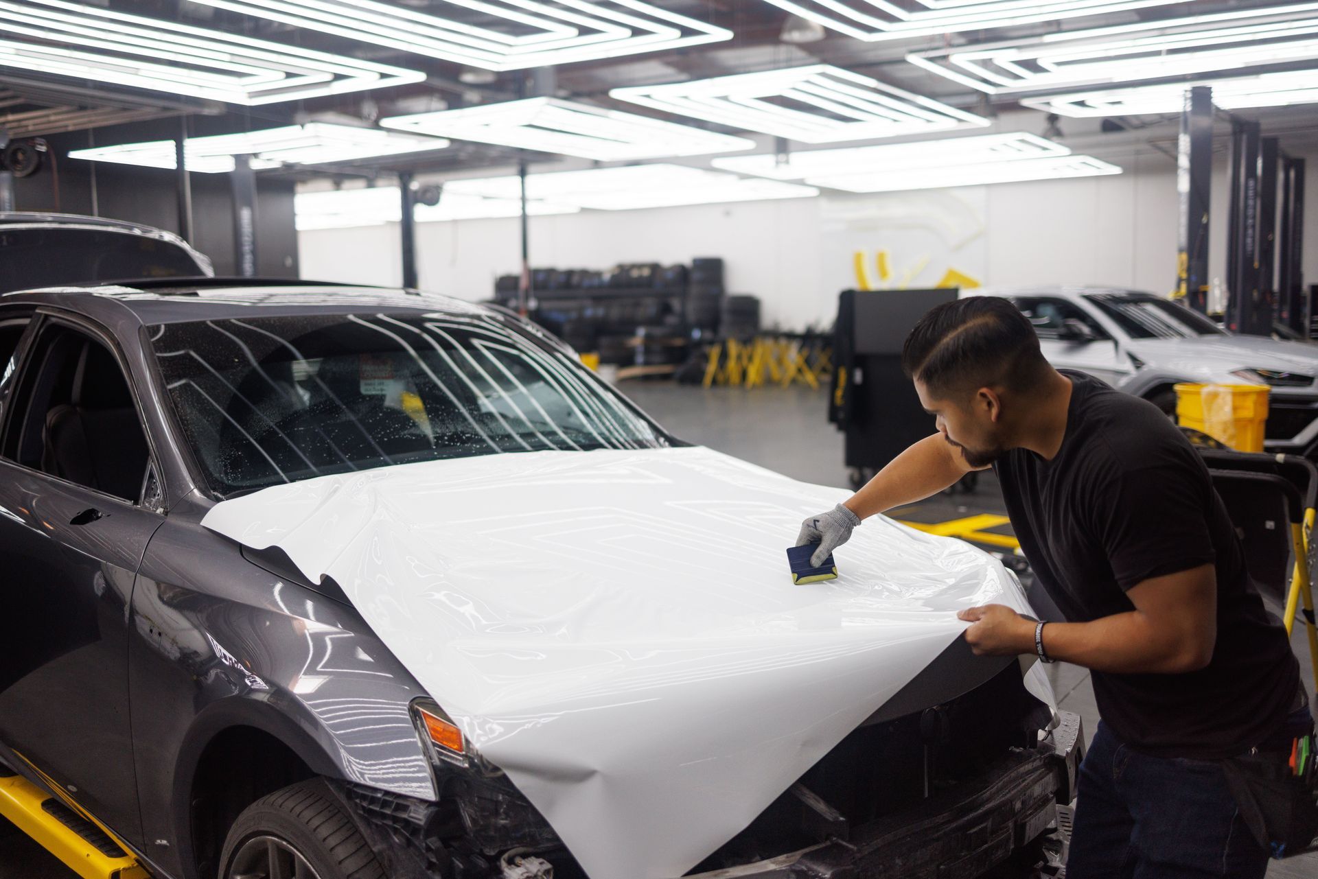 Person wrapping a black car hood with white vinyl in an auto shop