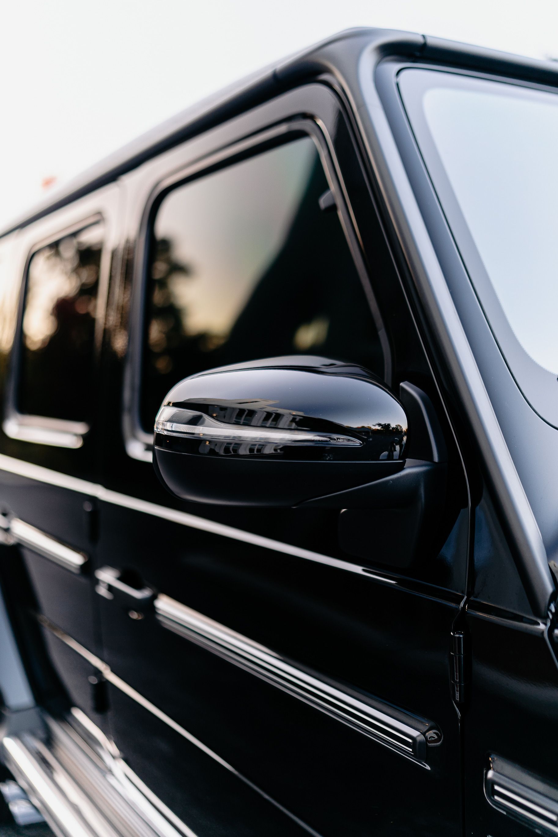 Close-up of a glossy black car’s side mirror and door in soft daylight