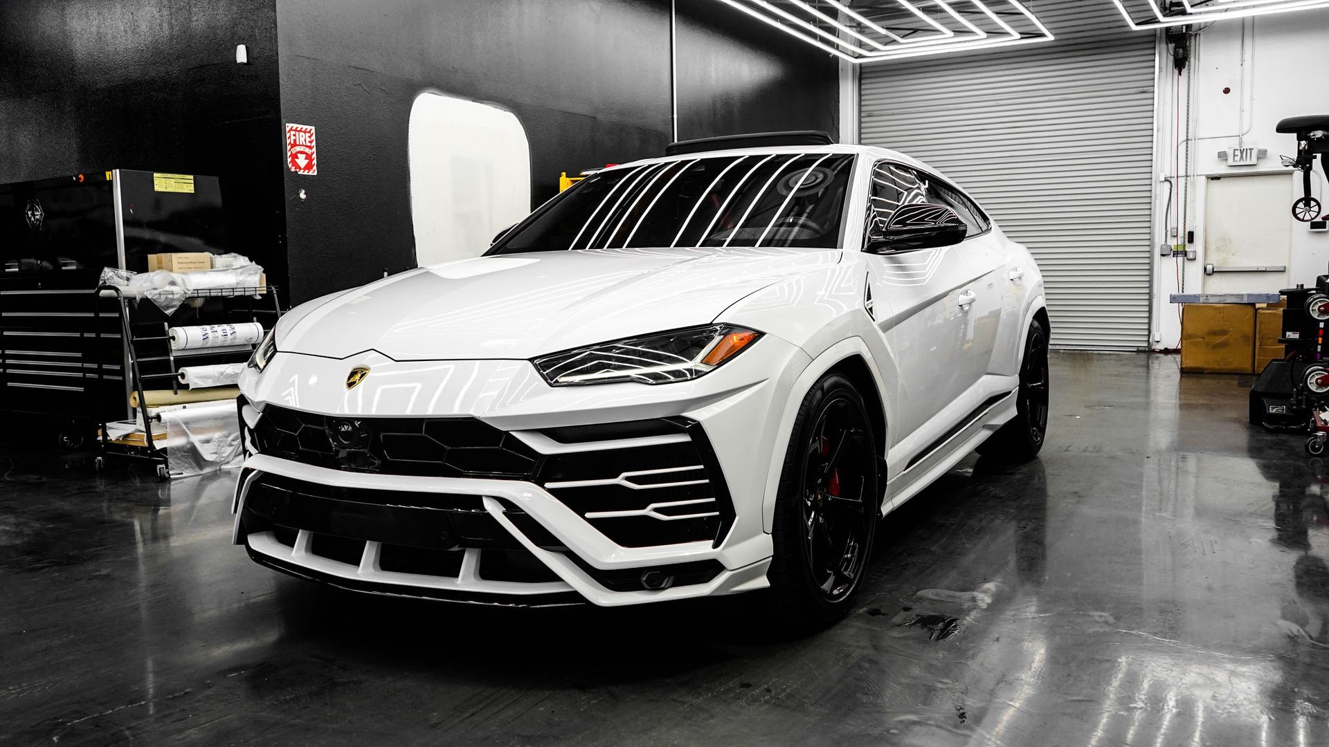 White Lamborghini SUV in a glossy showroom, front three-quarter view on a reflective black floor.
