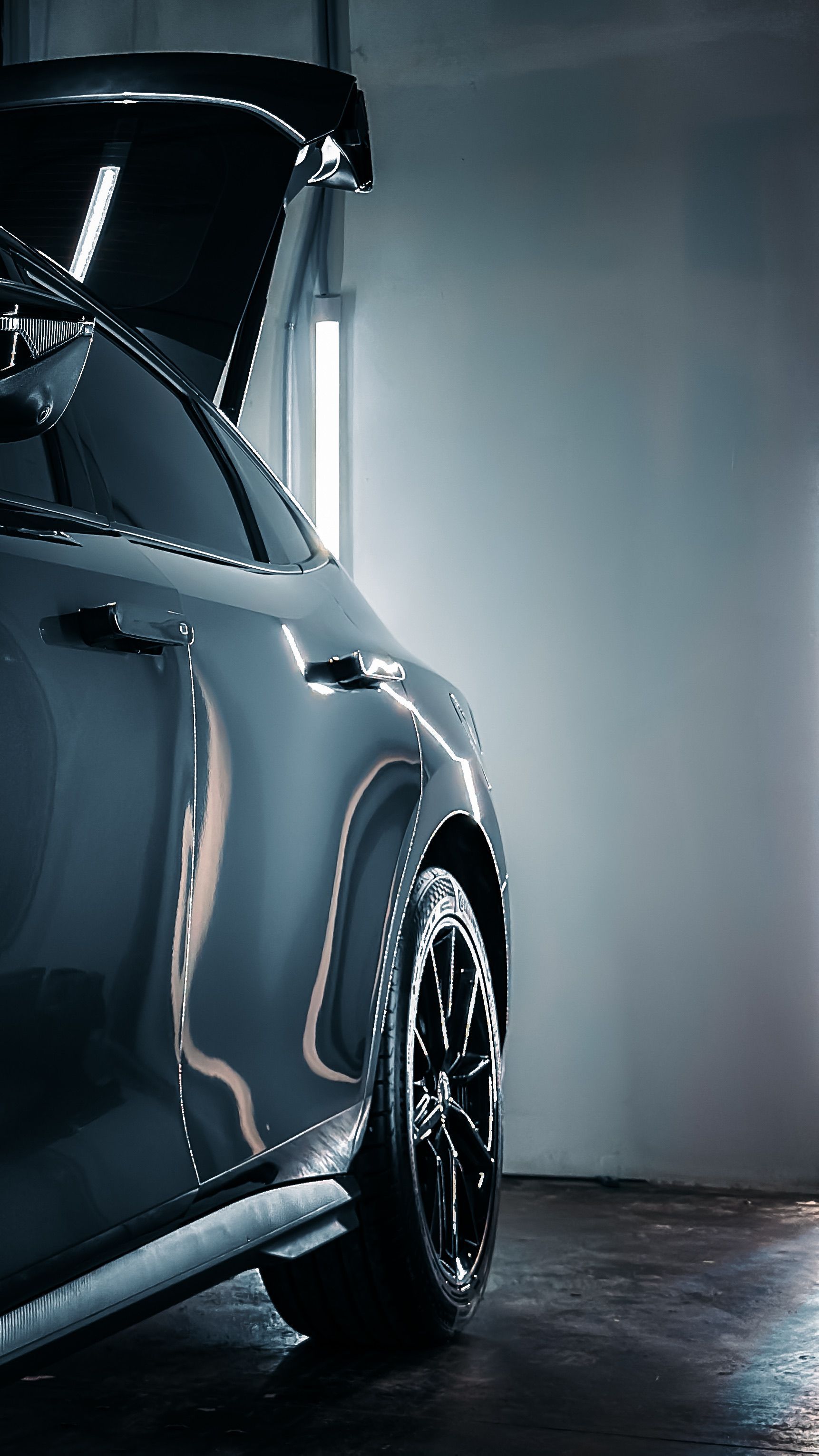Close-up of a dark blue sports car in a dim garage, showing the front side and wheel.