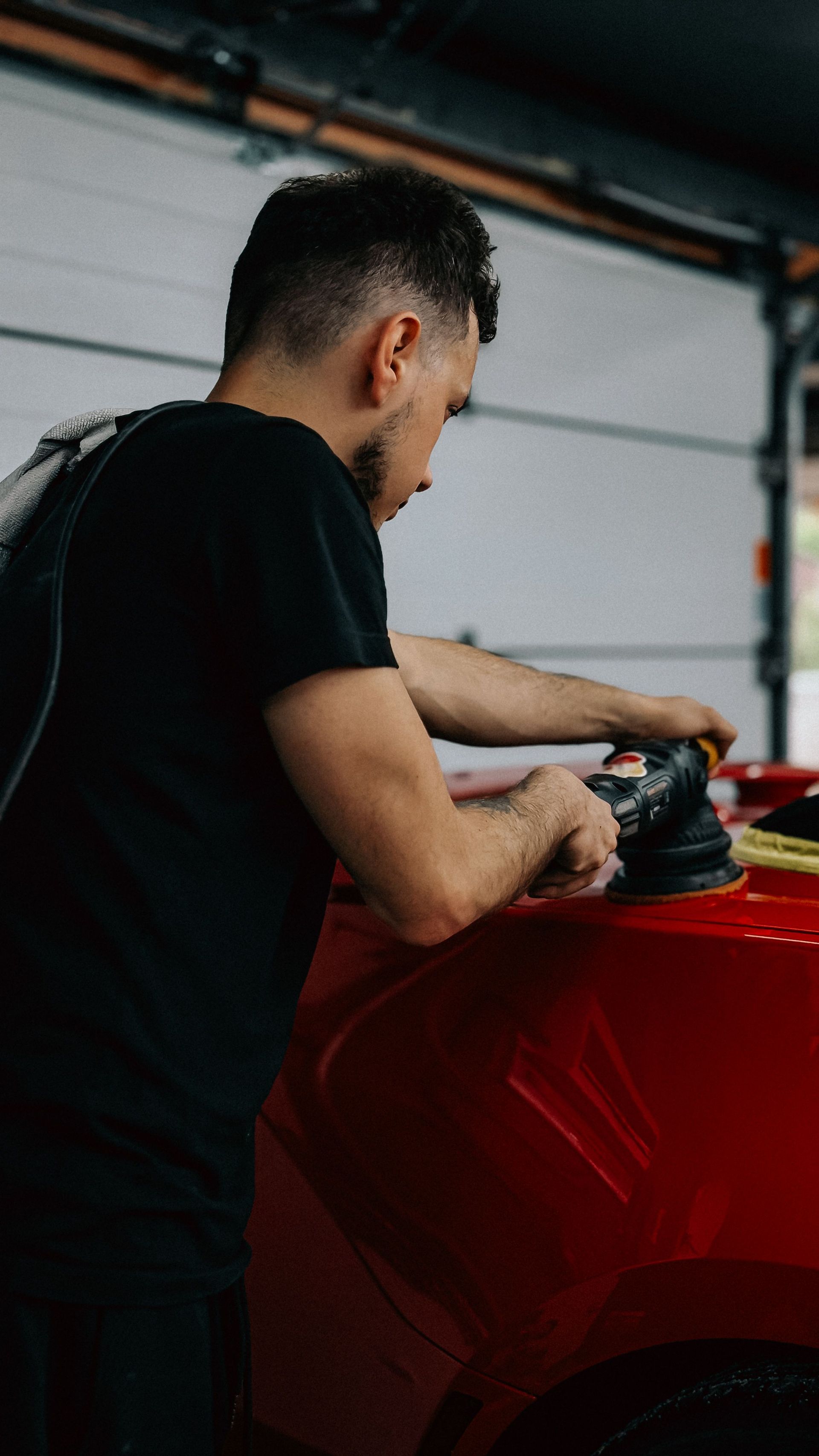 Man polishing a red car in a garage with a buffer tool