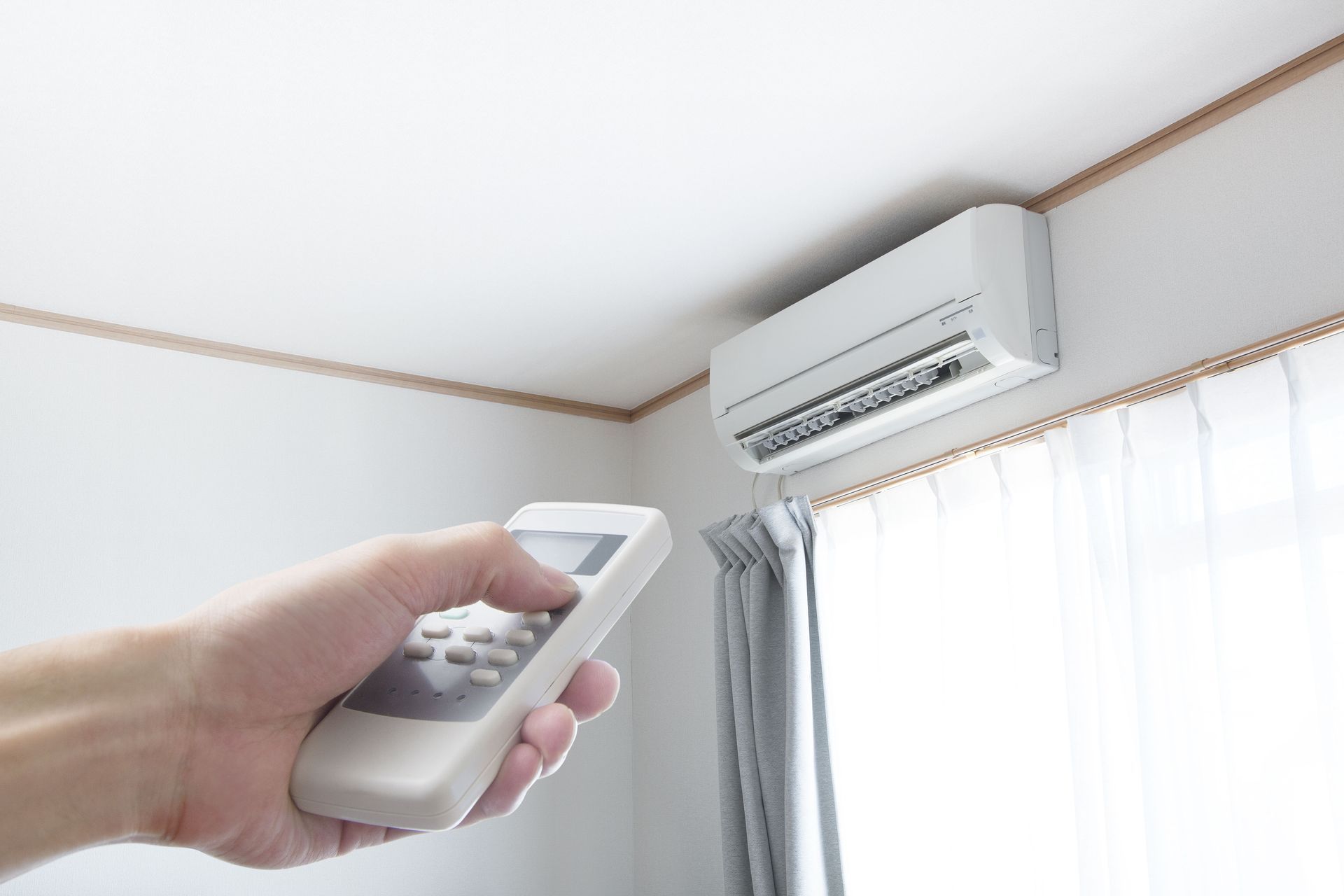 A person is holding a remote control in front of an air conditioner.