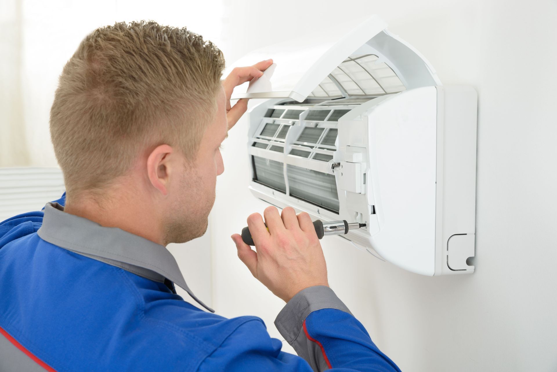 A man is fixing an air conditioner with a screwdriver.