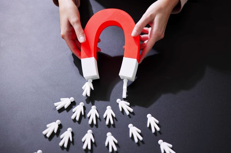 Hands holding a red horseshoe magnet pulling white stick figures on a dark surface