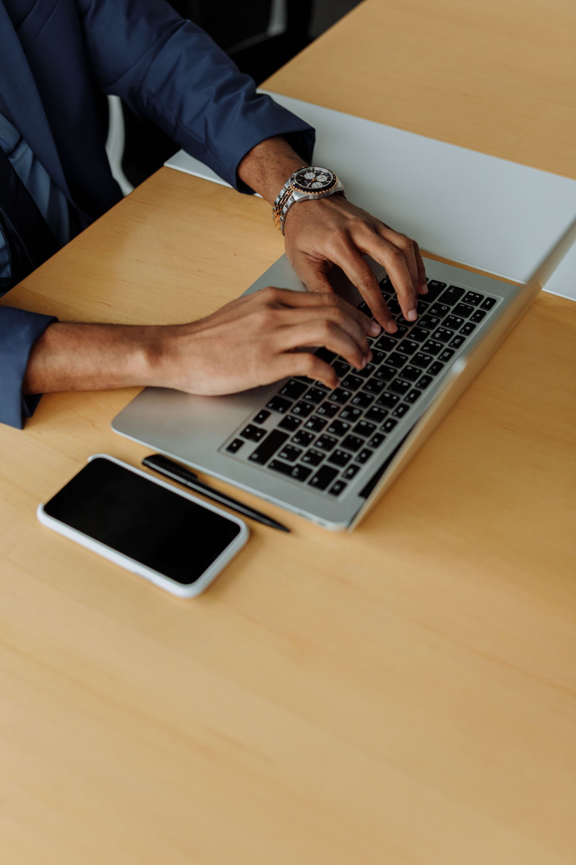 Hands typing on a laptop beside a smartphone on a wooden desk.
