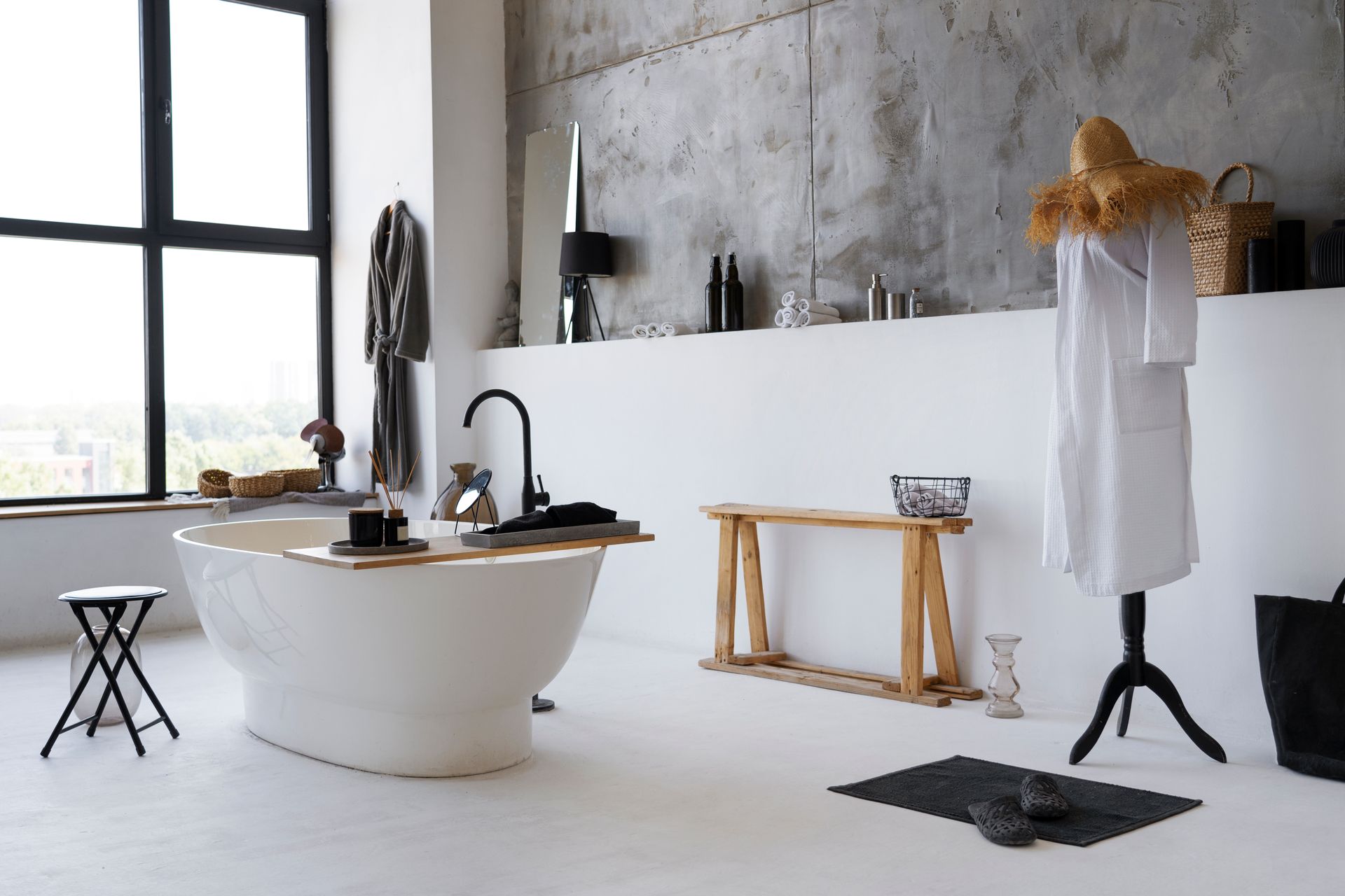 Minimalist bathroom with freestanding tub, black fixtures, wall-mounted towels, and large window light