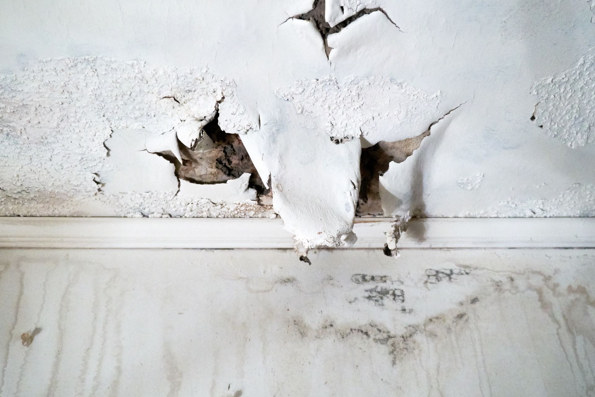 Water-damaged white ceiling with peeling paint and cracked plaster around a stain