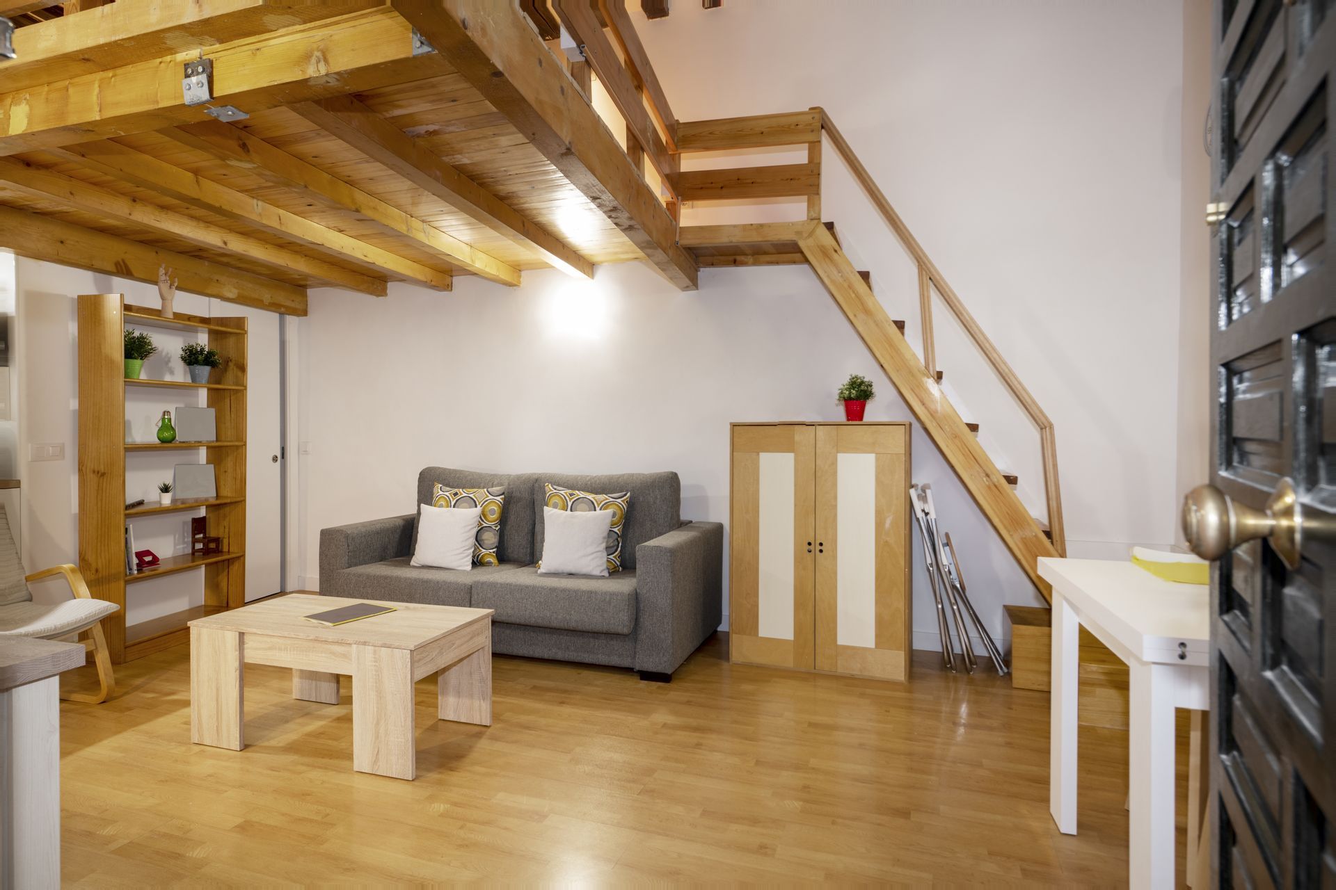 Modern loft living room with wood floors, gray sofa, staircase, and light wood coffee table