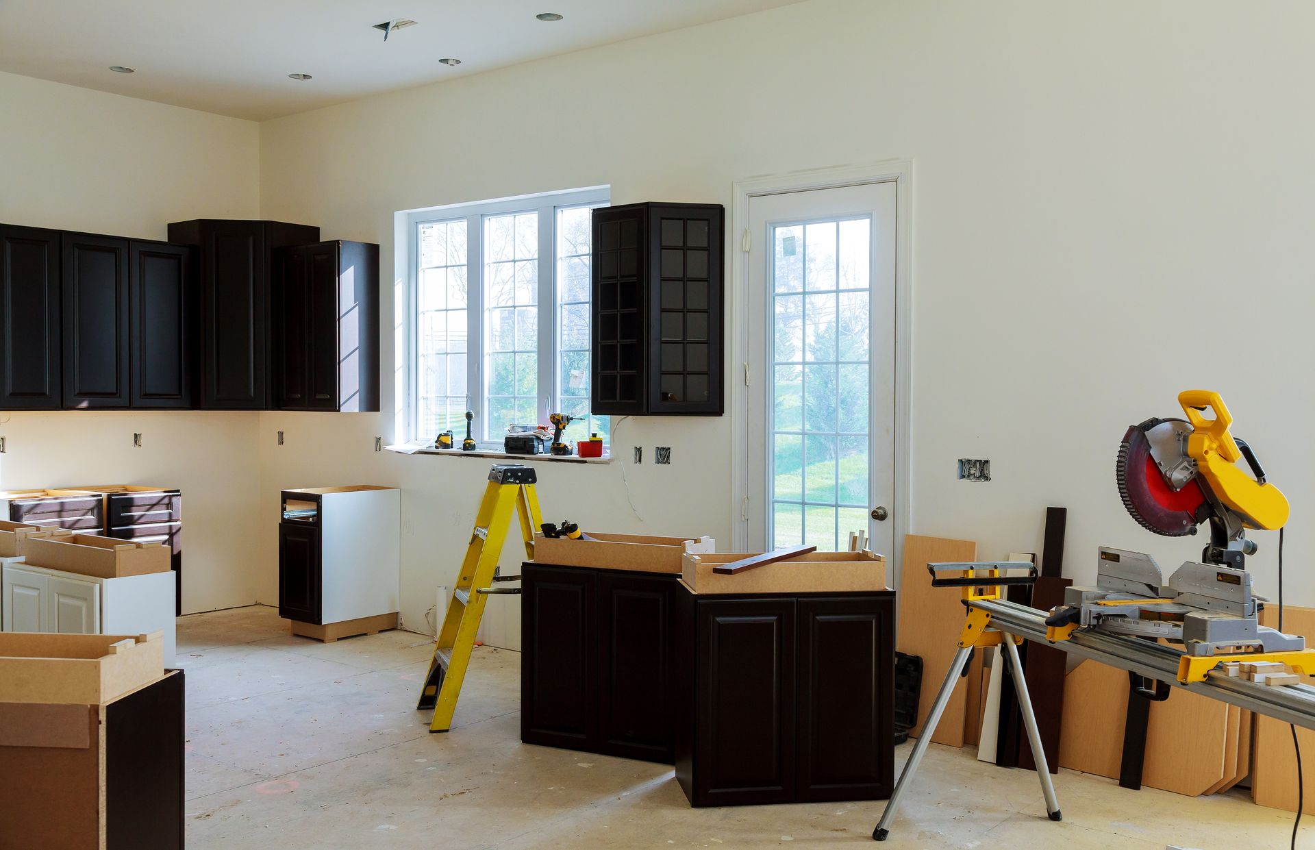 Kitchen under renovation with cabinets, boxes, tools, and a saw on a stand