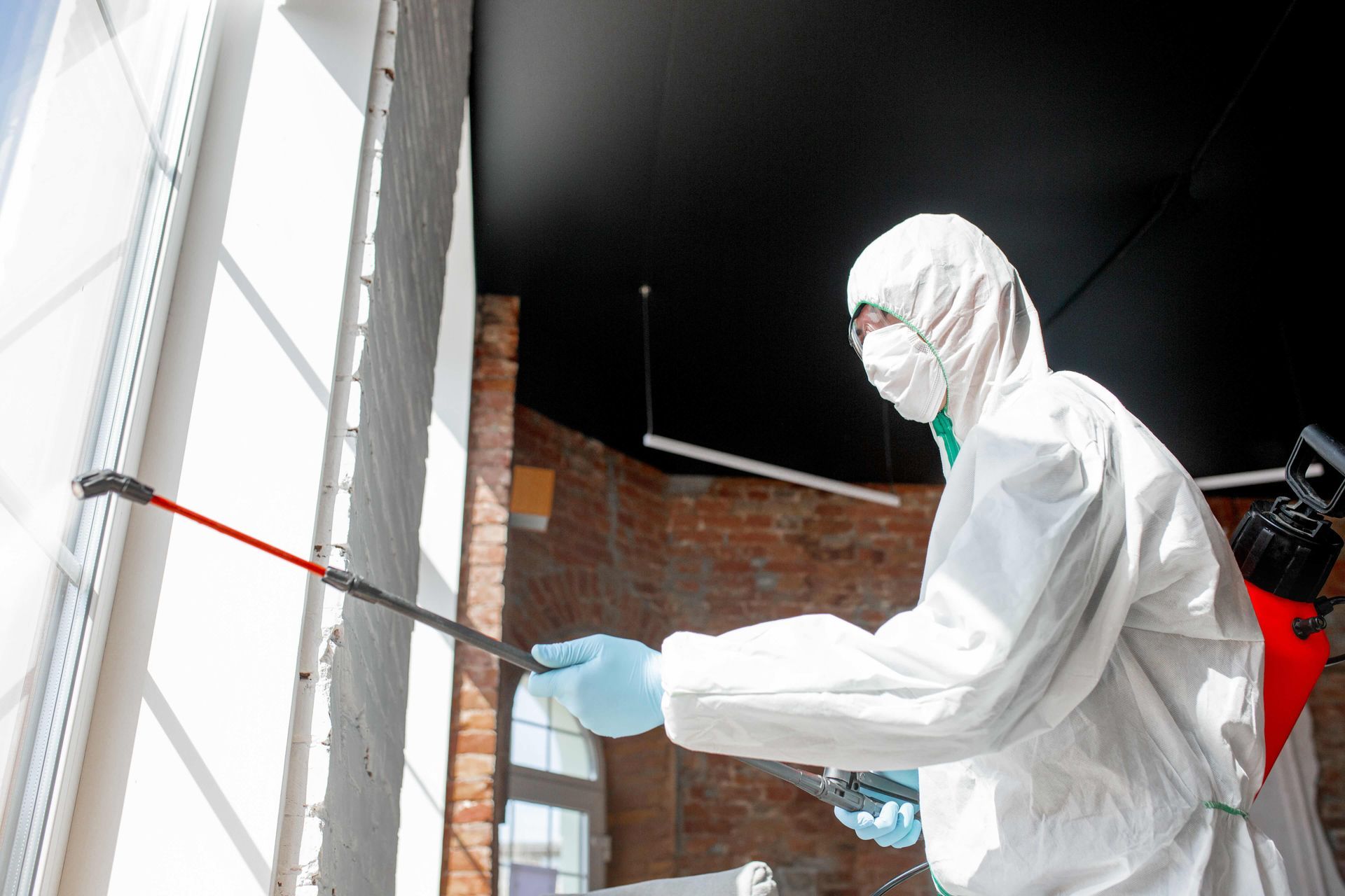 a man in a protective suit is spraying a window with a sprayer .