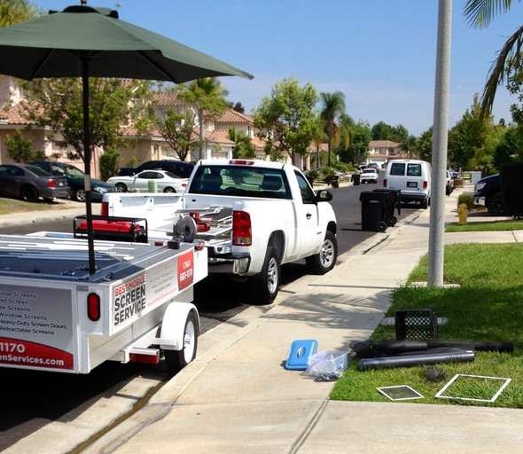 A white truck is parked next to a trailer that says screen service
