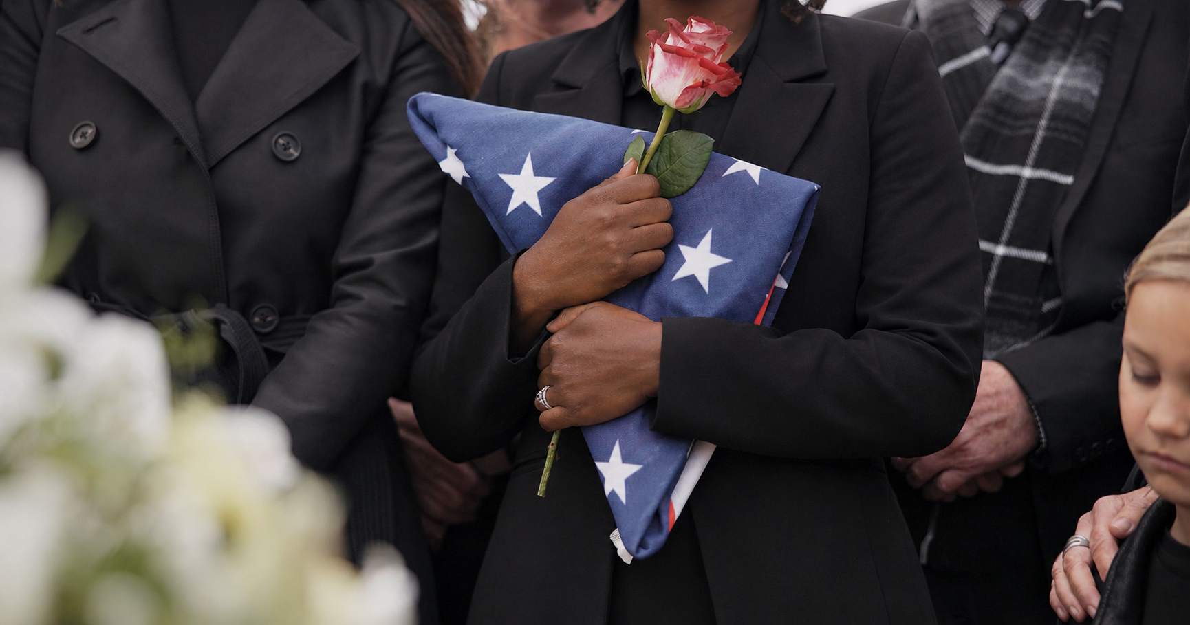 A woman is holding an american flag and a rose at a funeral.
