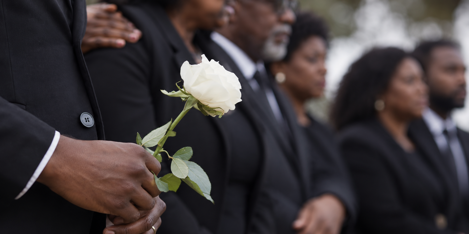 A man is holding a white rose in his hand at a funeral.