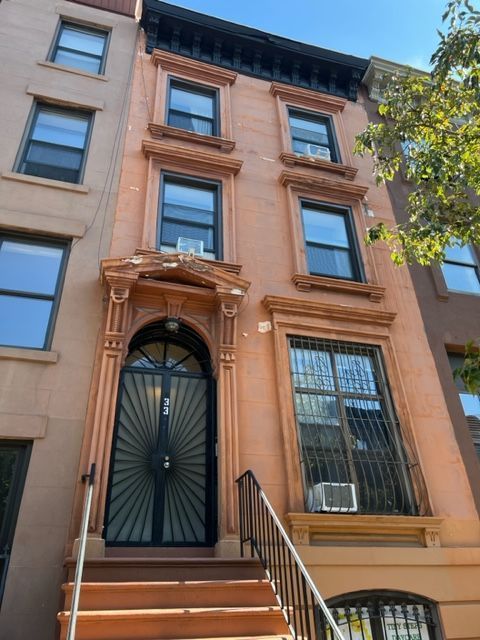 Brownstone townhouse facade with stoop, black front door, and large windows on a sunny street