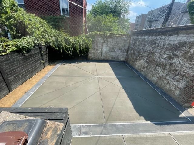 Empty concrete backyard patio beside brick walls and greenery, seen in bright daylight