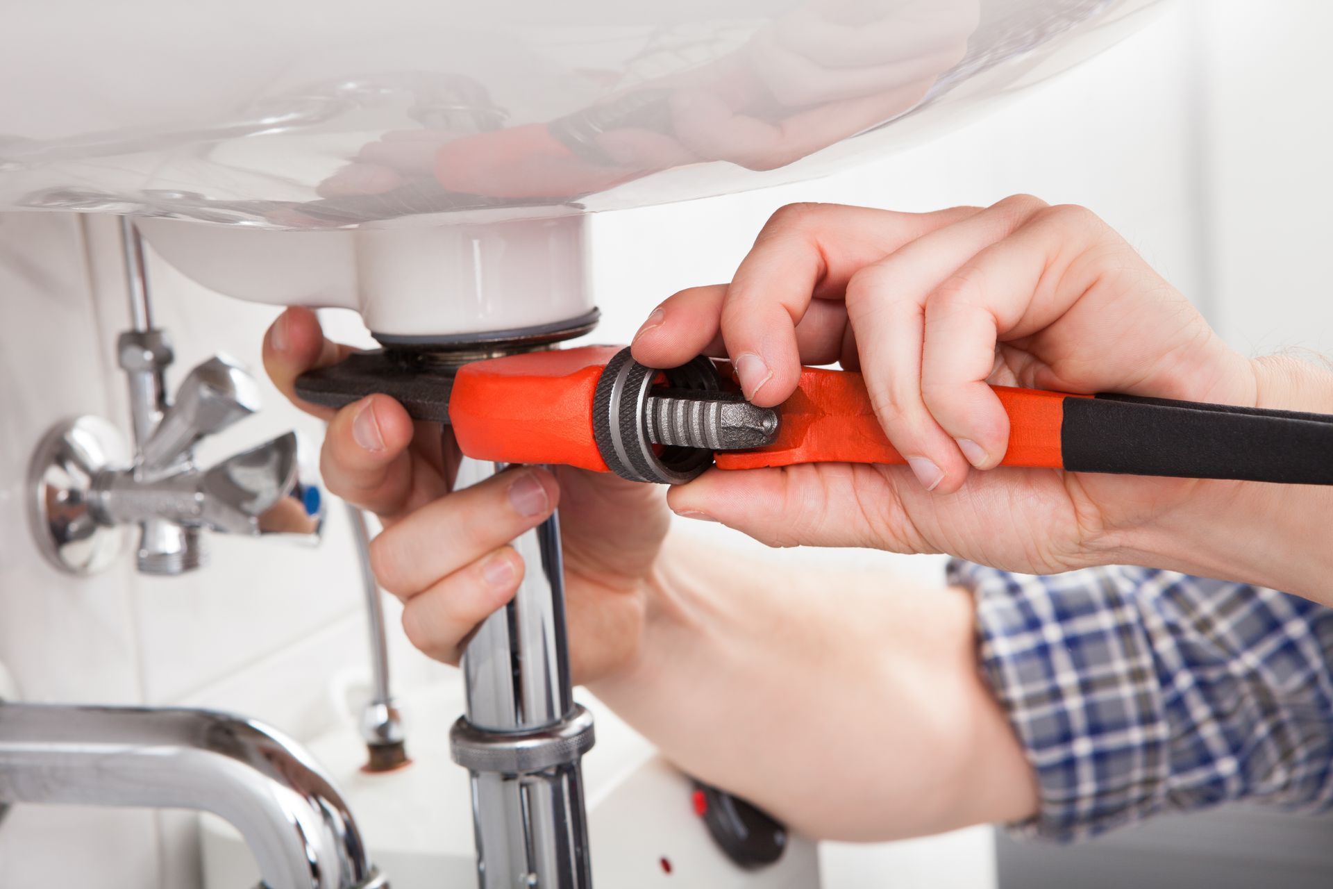 A plumber is fixing a sink with a wrench.