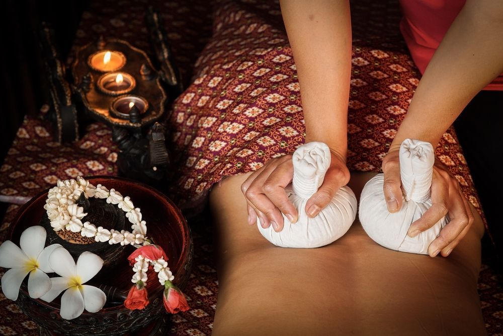 Hands Using Hot Herbal Compress on a Person's Back — Leela Thai Massage & Spa in Newtown, QLD