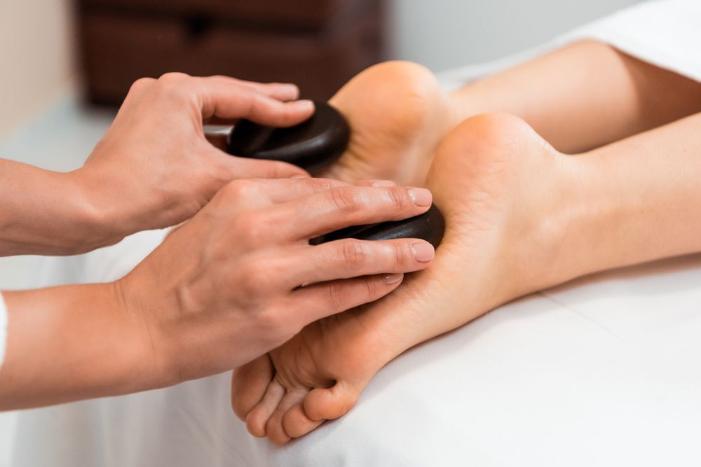 Hands Massaging Feet With Hot Stones on a White Spa Table — Leela Thai Massage & Spa in Newtown, QLD